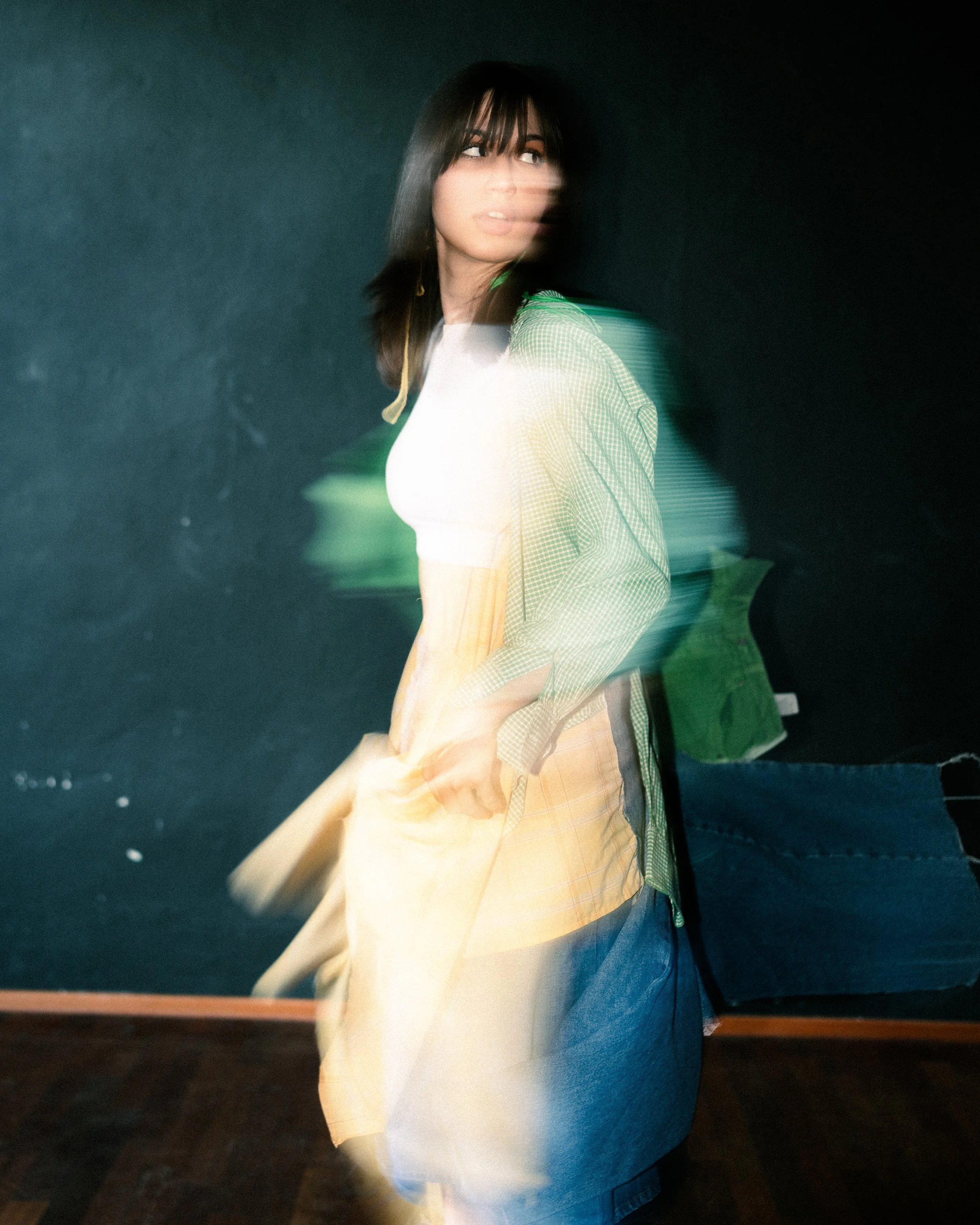 A woman with dark hair and bangs standing in front of a blackboard, with a motion blur effect.