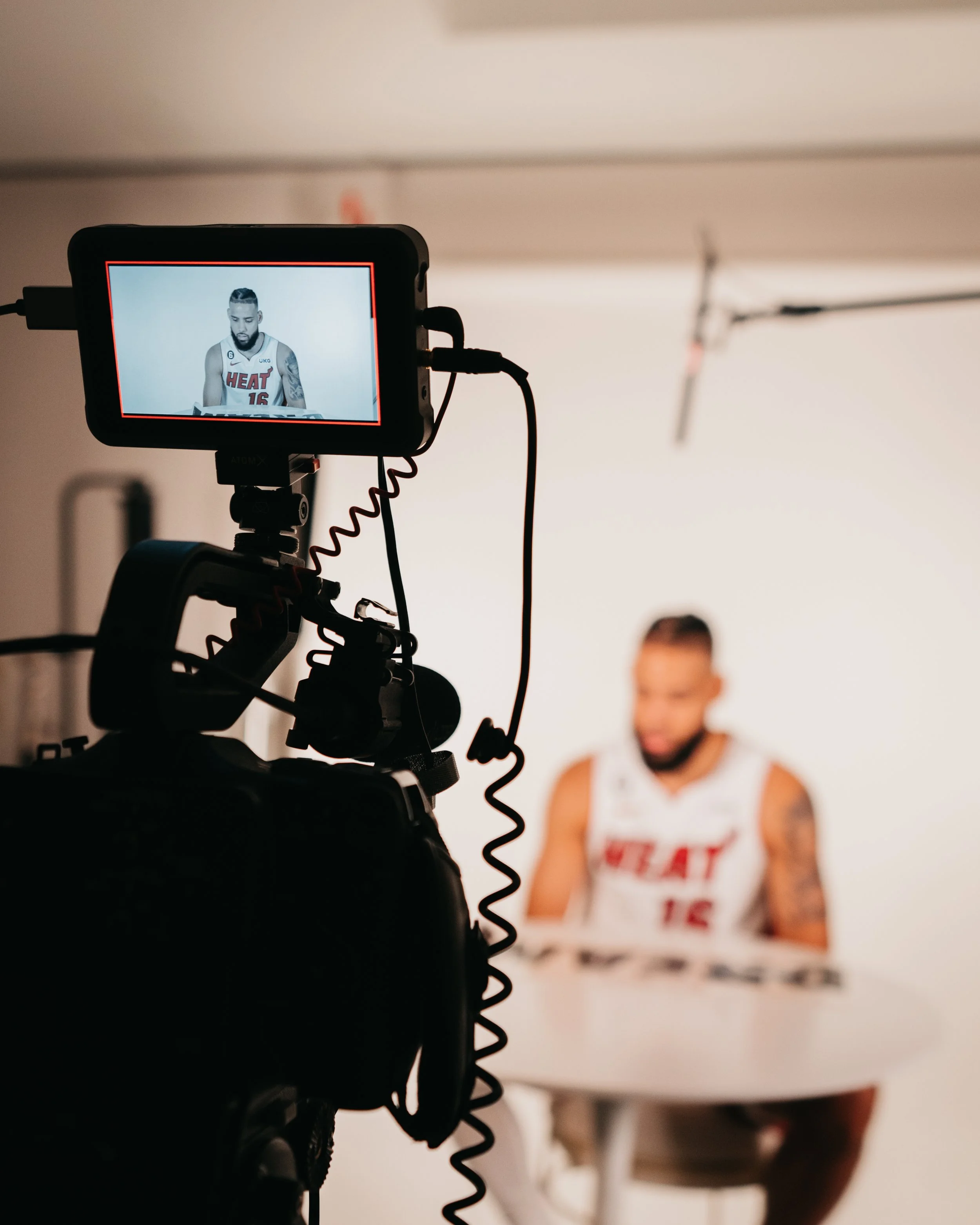 A person in a Miami Heat basketball jersey is being filmed in front of a white background.