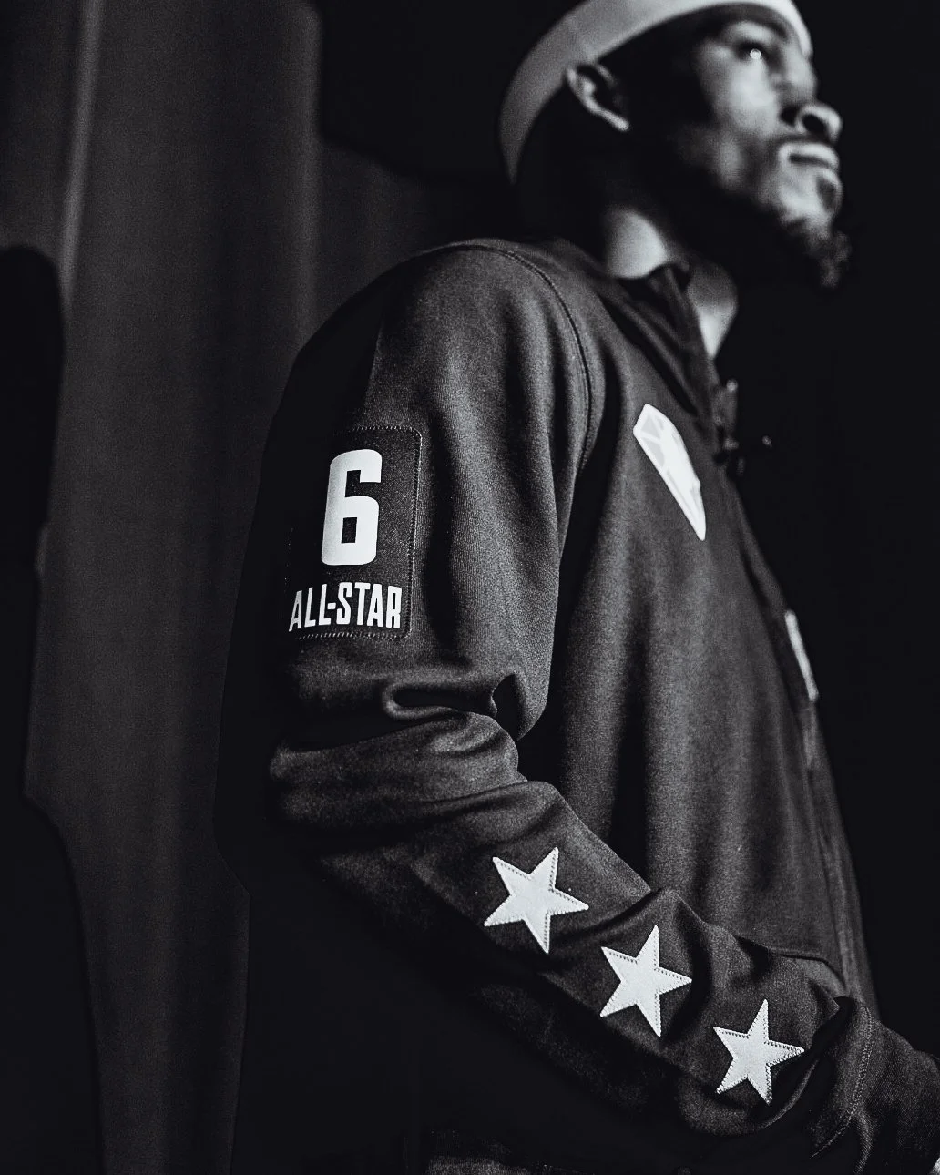 Black and white photo of a man wearing a captain's hat and a dark jacket with patches, including the number 6 and the words 'ALL-STAR' on the sleeve, sitting in a relaxed pose.