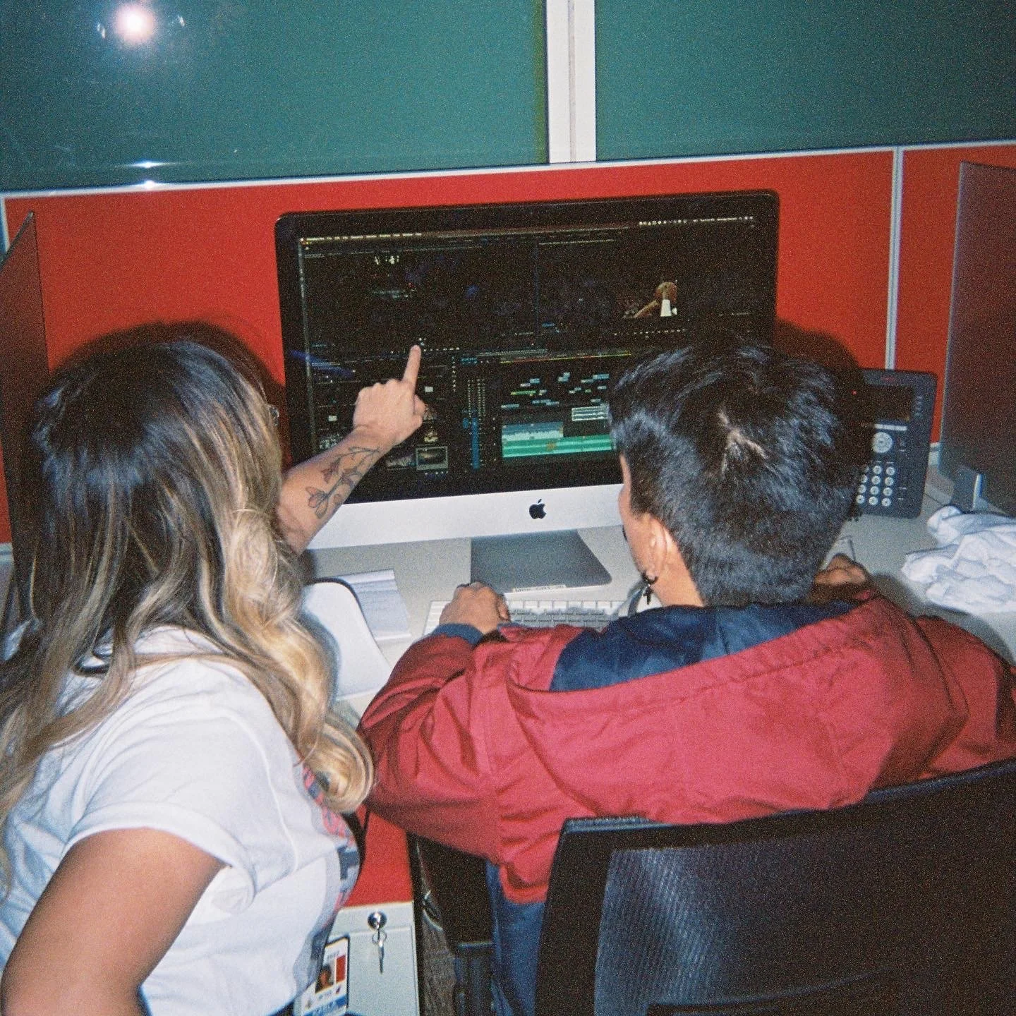 Two people working together on a computer, with one person pointing at the screen, which displays video editing or graphic design software.
