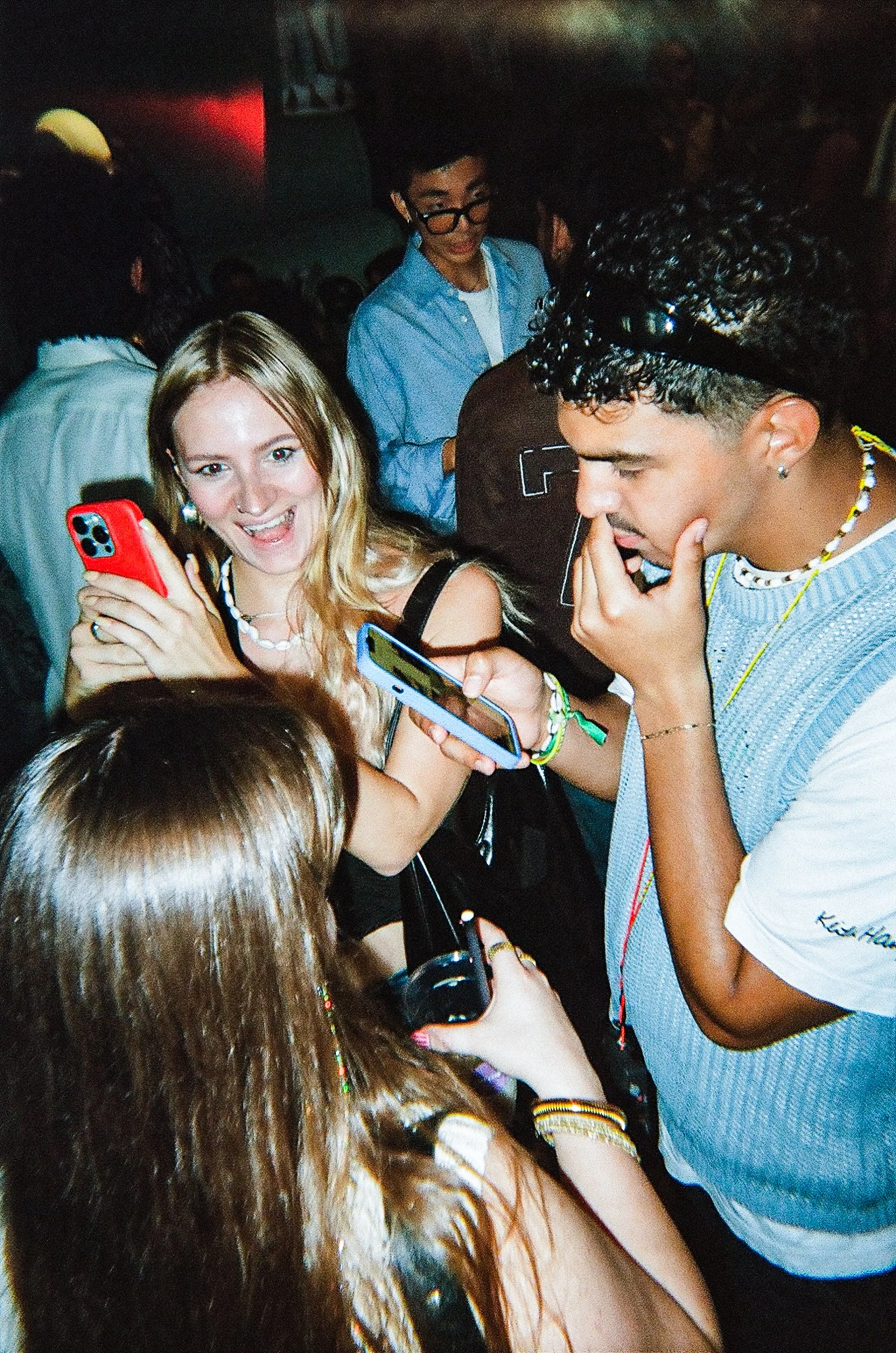 A group of young people at a crowded party or event, looking at their smartphones and having fun.