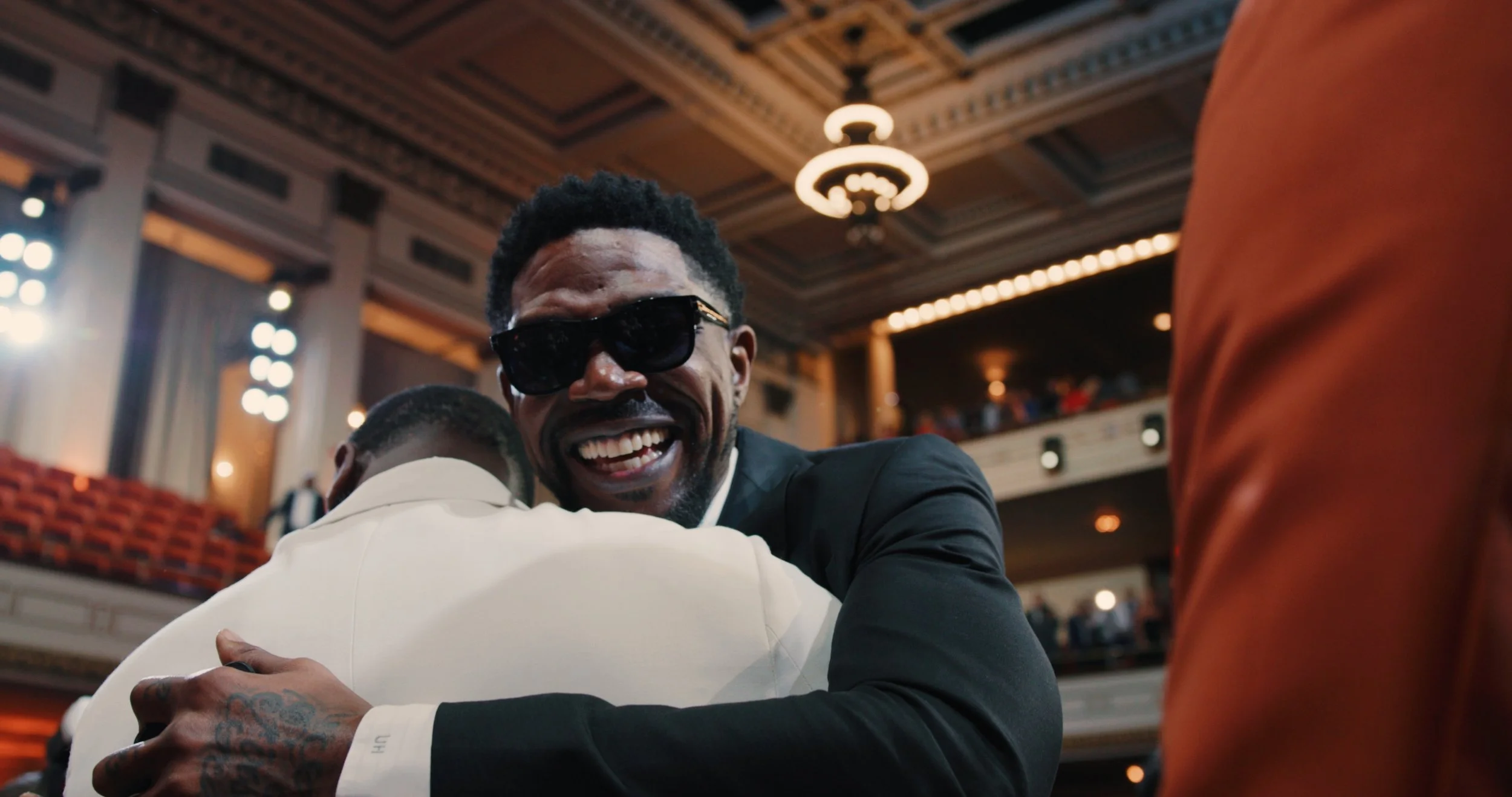 Udonis haslem hugging another person in a large indoor venue with ornate ceiling details and warm lighting.