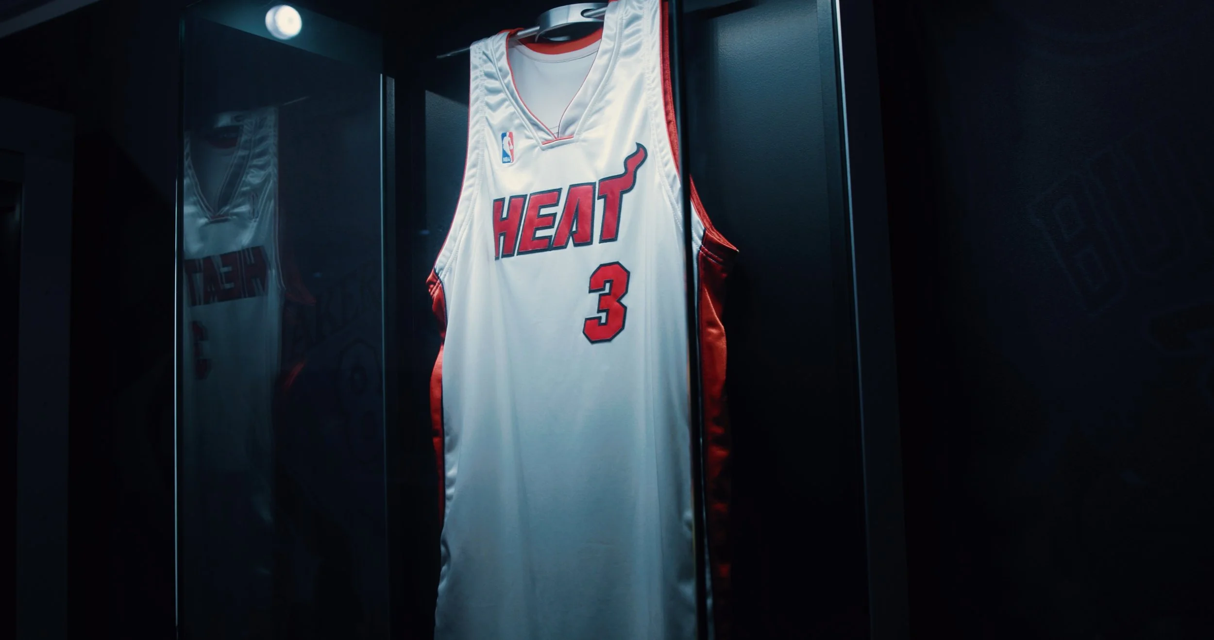 Miami Heat basketball jersey with the number 3 hanging inside a glass display case.