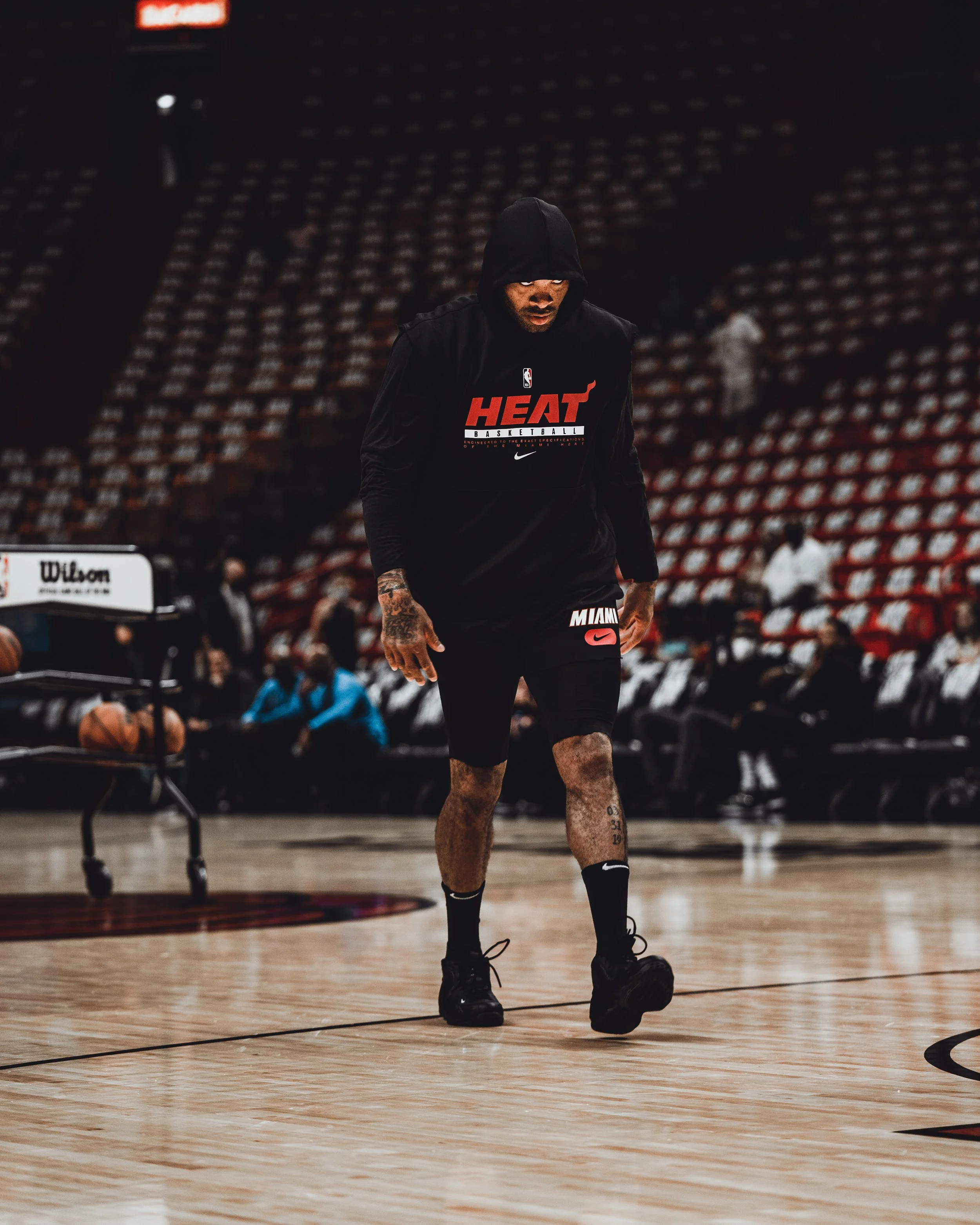 A basketball player wearing a hoodie and shorts practicing on an empty basketball court.