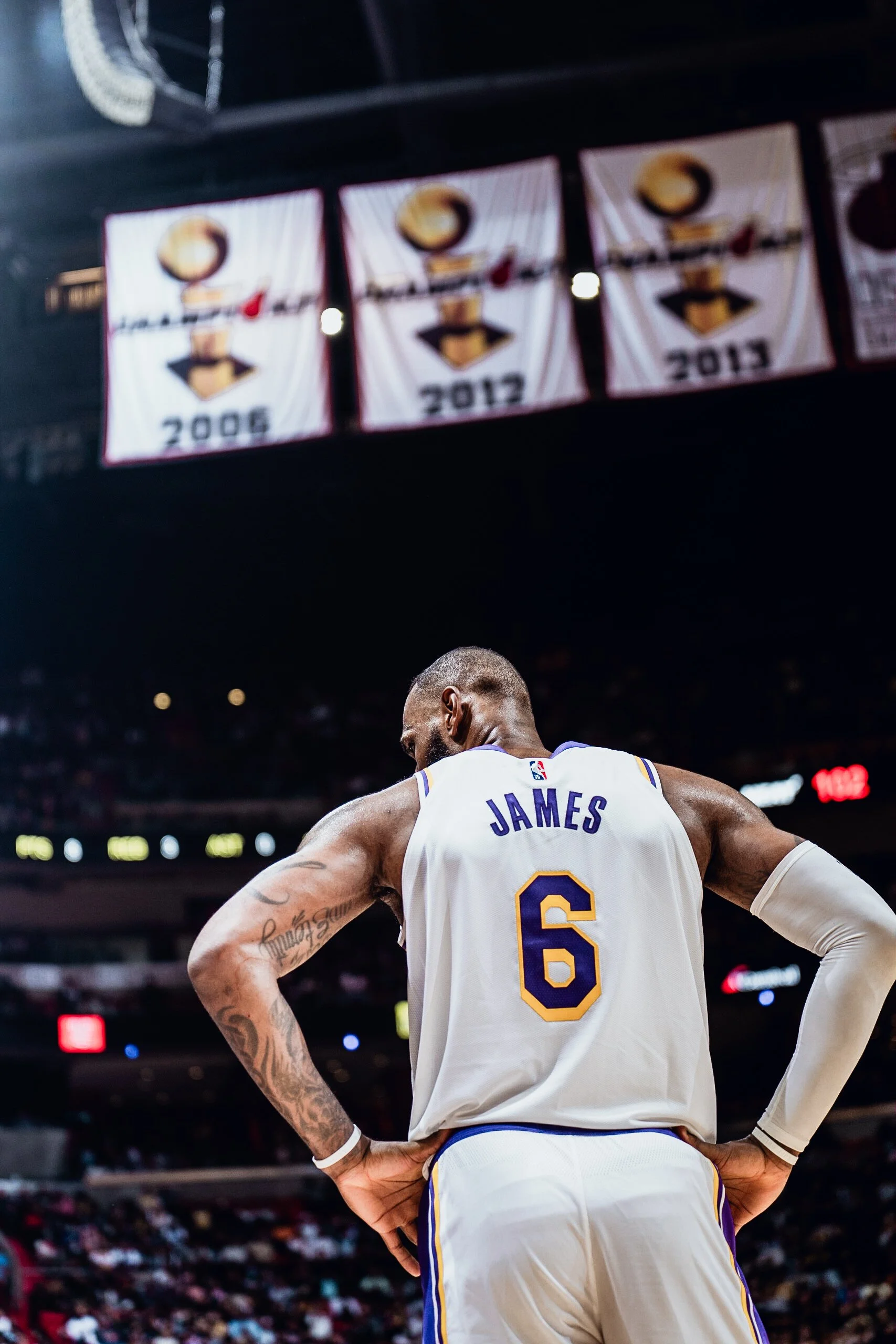 A basketball player wearing a white jersey with the name 'James' and the number 6 is standing on the court, viewed from behind with his hands on his hips.