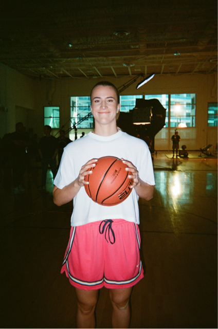 Young woman in a white t-shirt and pink shorts holding a basketball in an indoor gym.