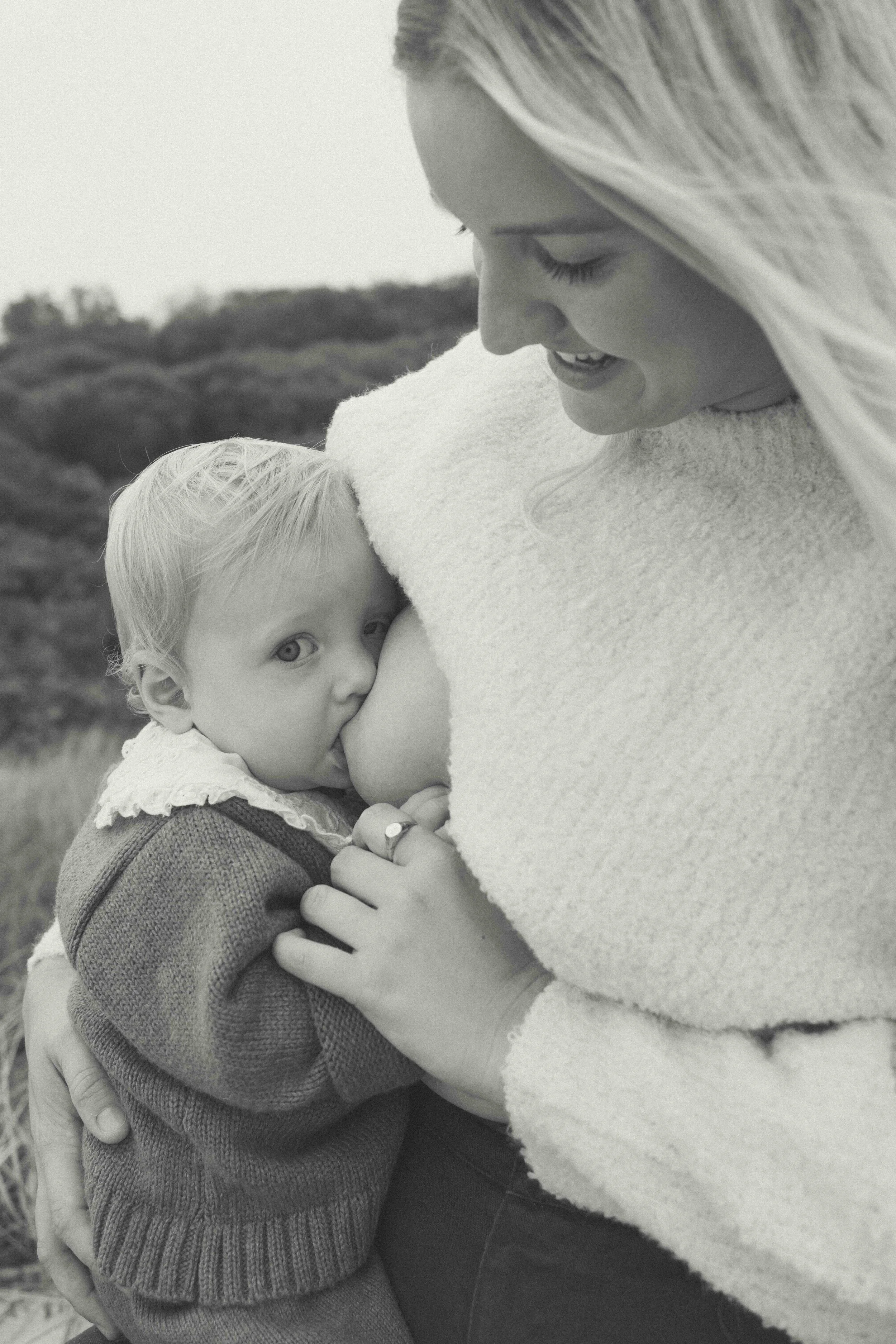A woman with long hair hugging a young girl with short blonde hair outdoors, close-up side view in black and white.