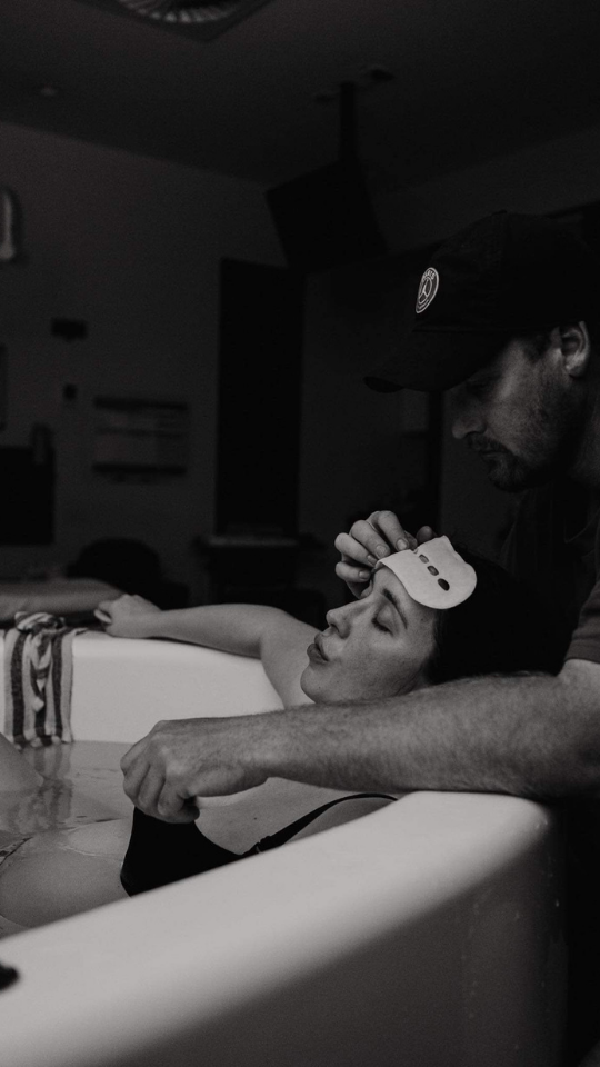 A person receiving a religious or spiritual cleansing or blessing in a dark indoor setting, with another person performing a ritual or prayer.