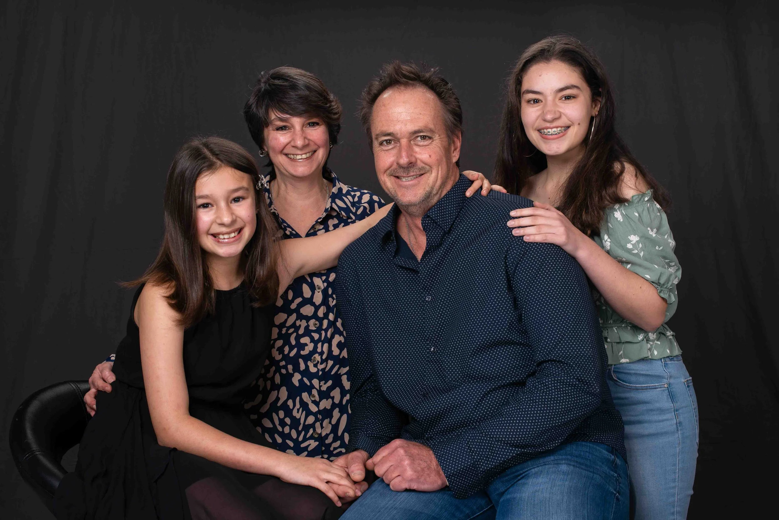 Family portrait of a man, woman, and three young girls smiling against a dark background.