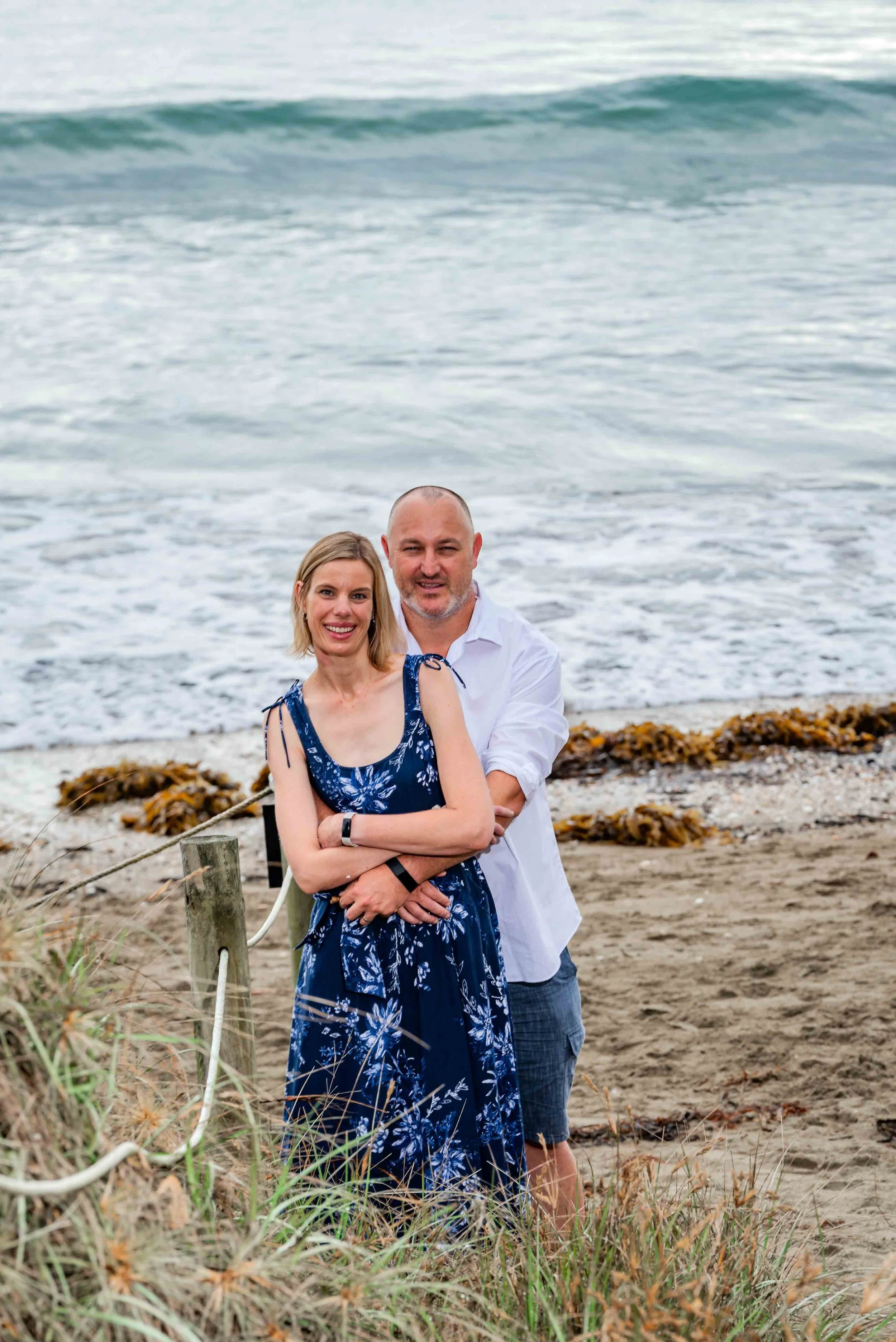 A smiling couple embracing on a beach with ocean waves in the background.