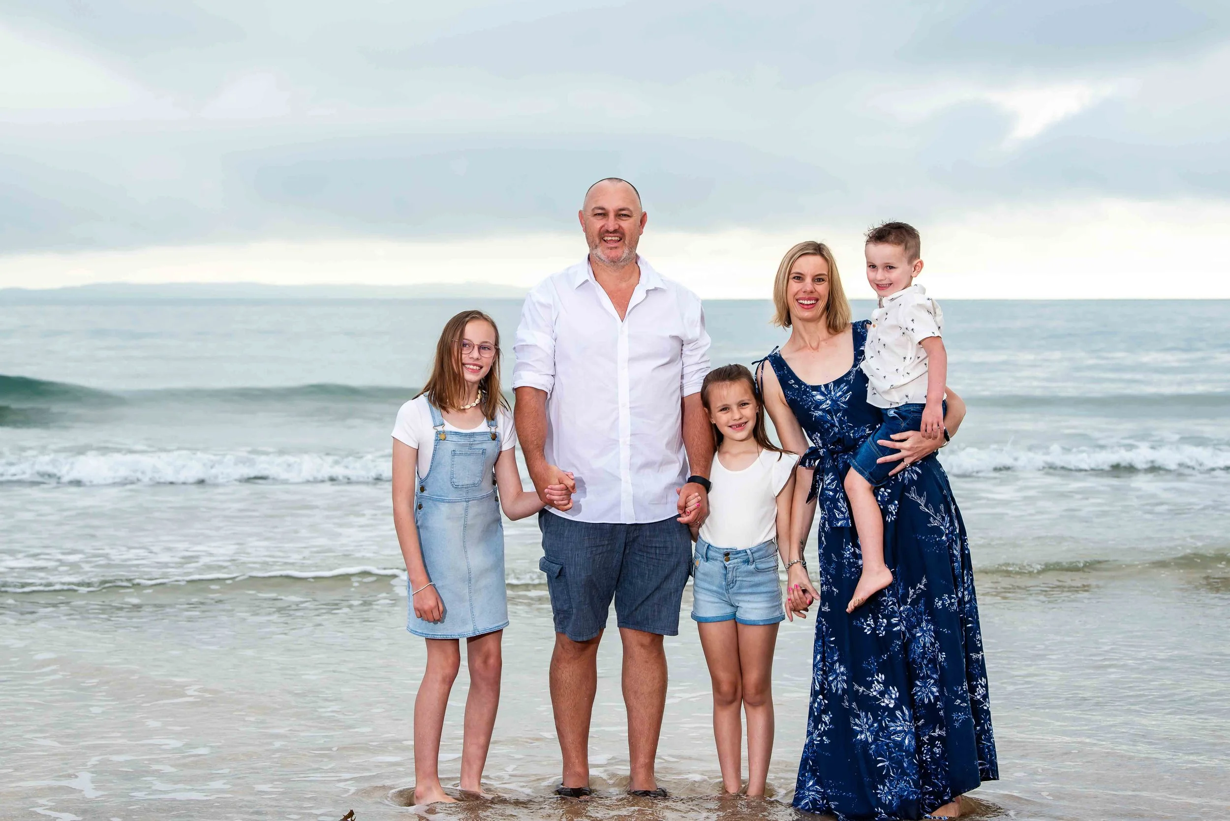 Family of six standing on the beach with ocean in the background, smiling and holding hands