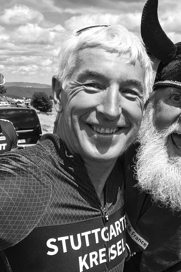 Man in red cycling jersey taking a selfie with a person wearing a red devil costume with horns, outdoor setting.