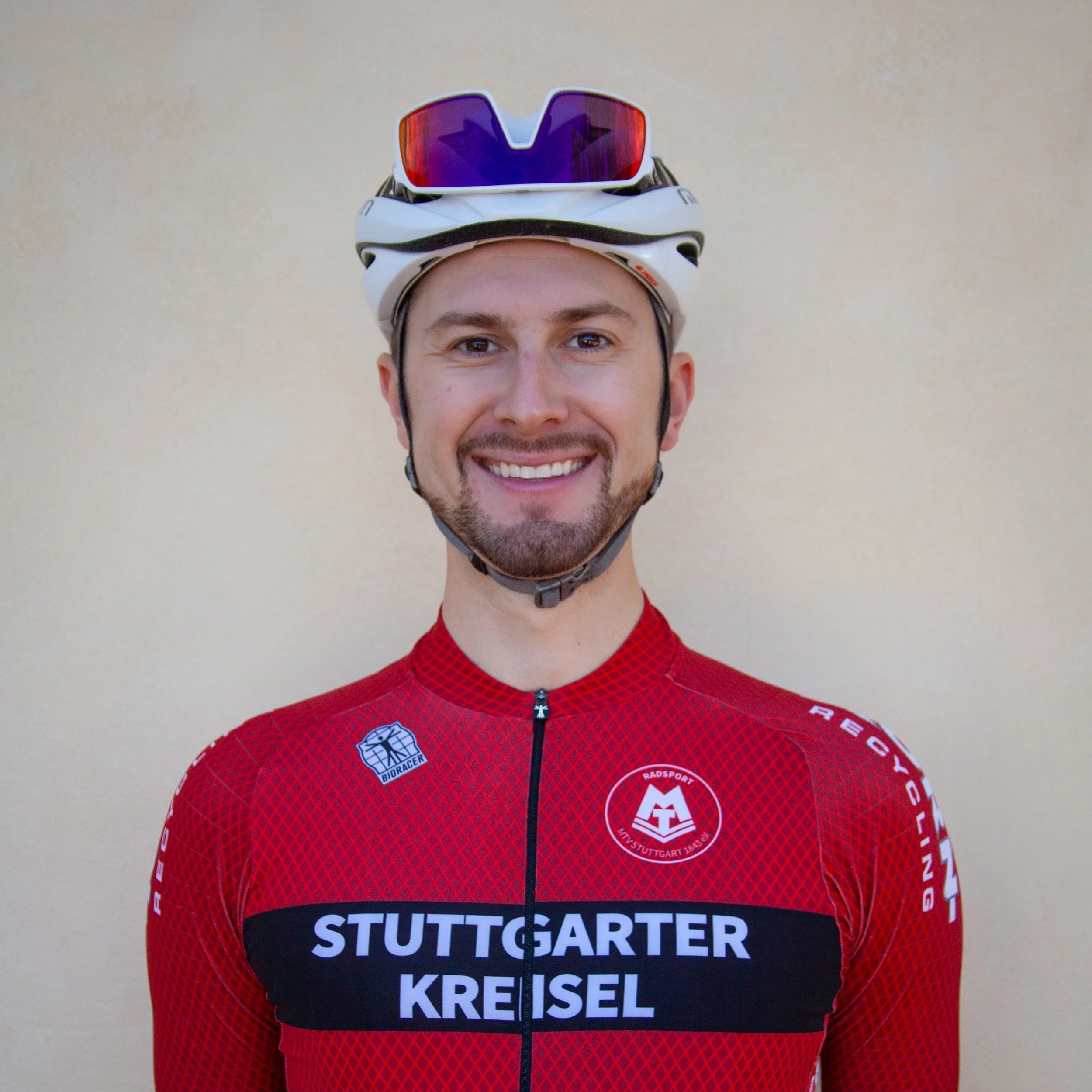 Person wearing a red cycling jersey with a white helmet, smiling on a city street.