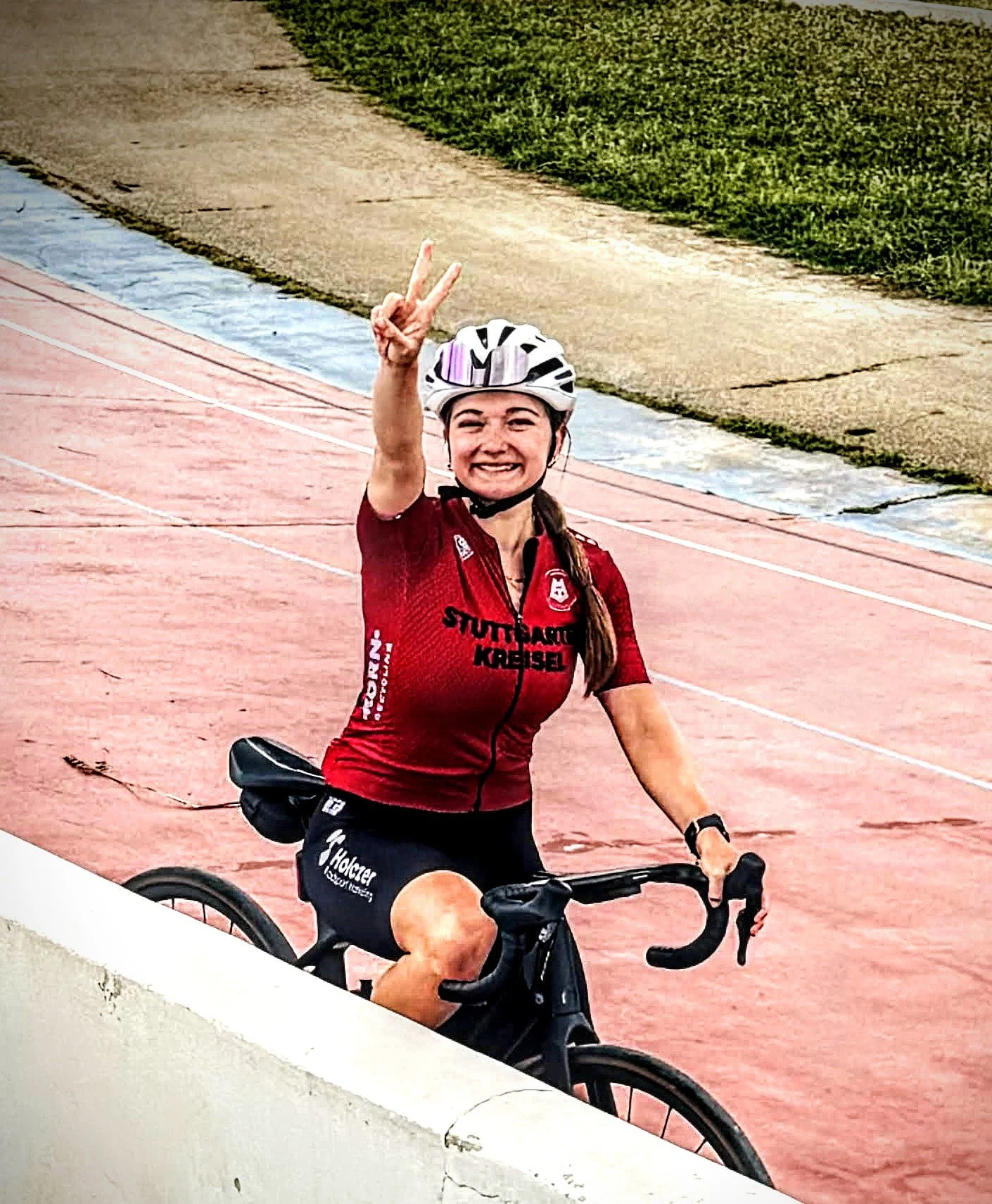 Cyclist smiling with helmet and red cycling jersey near a lake with mountains in the background.