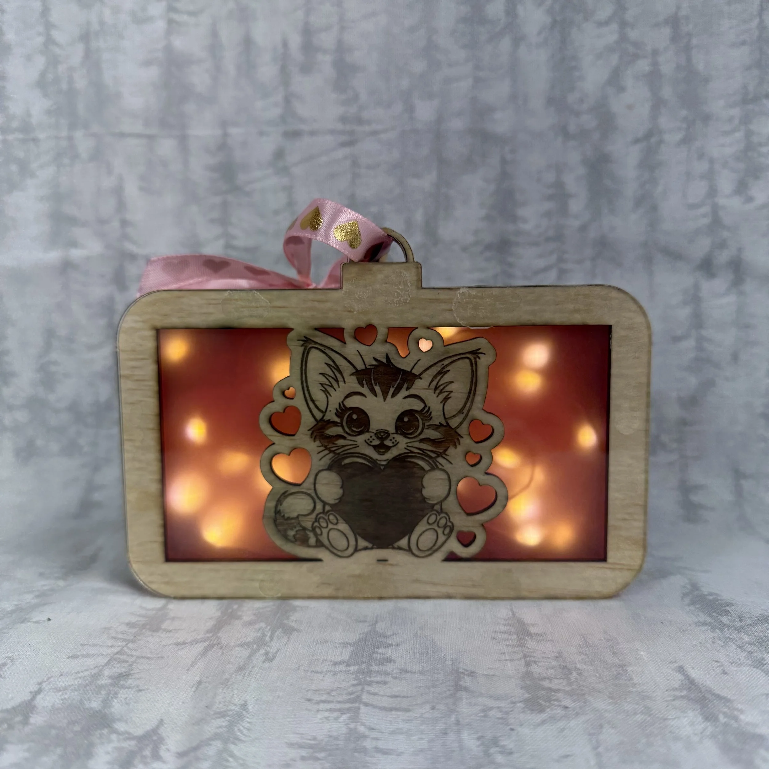 Wooden photo frame with a cute cartoon kitten holding a heart, decorated with smaller hearts, and illuminated with soft glowing lights behind.