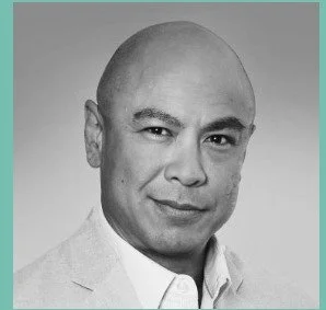 Black-and-white portrait of a bald man wearing a suit jacket and collared shirt, looking at the camera with a slight smile.
