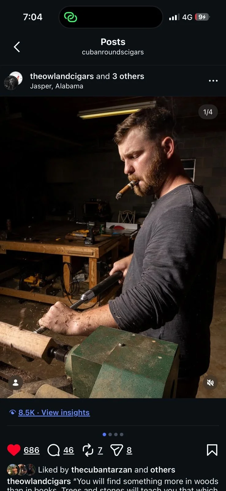 Man in a gray shirt with a beard and a cigar in his mouth, using a woodworking tool in a workshop.
