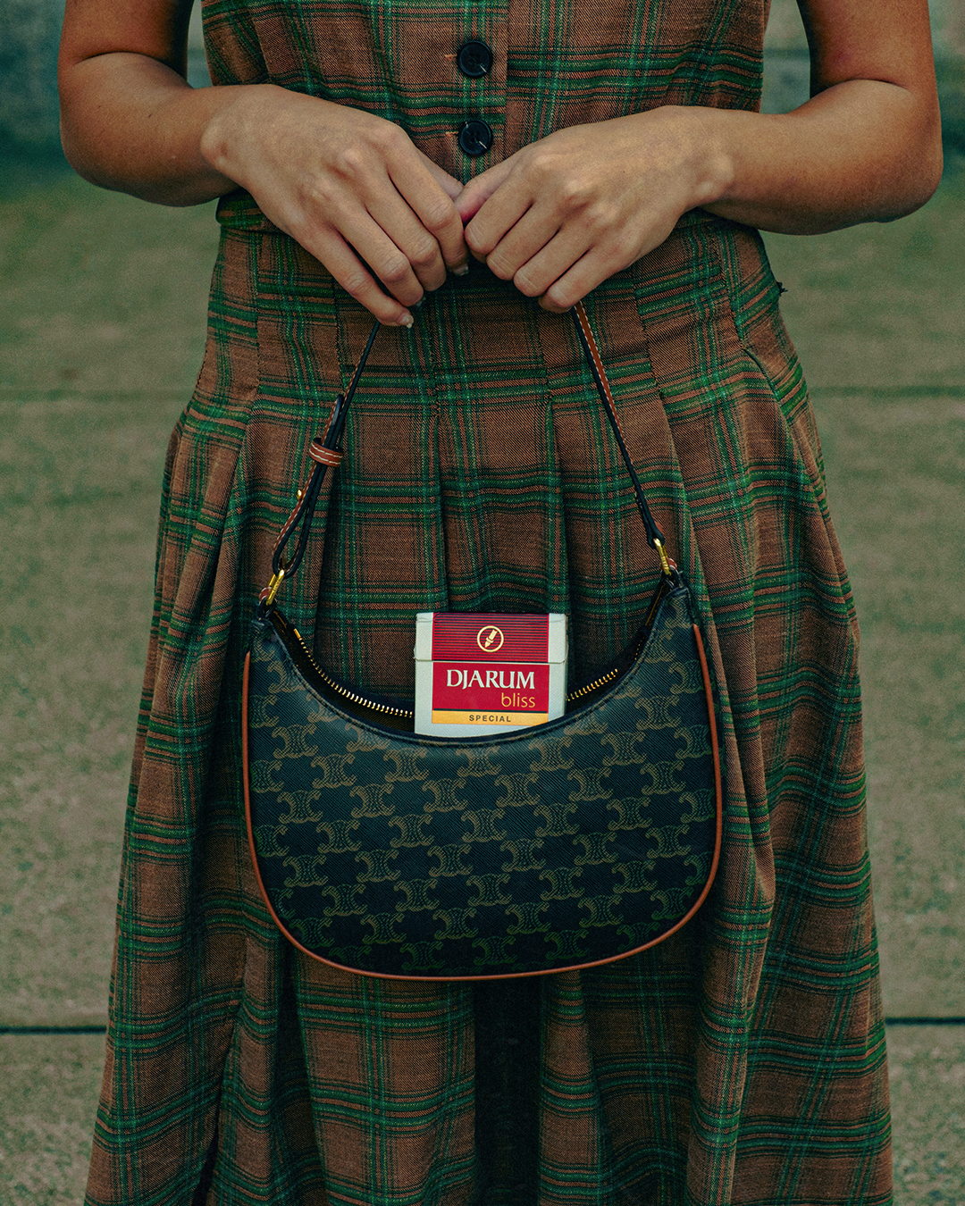 A woman in a plaid brown and green skirt holds a purse with a pack of Djarum Bliss cigarettes inside.