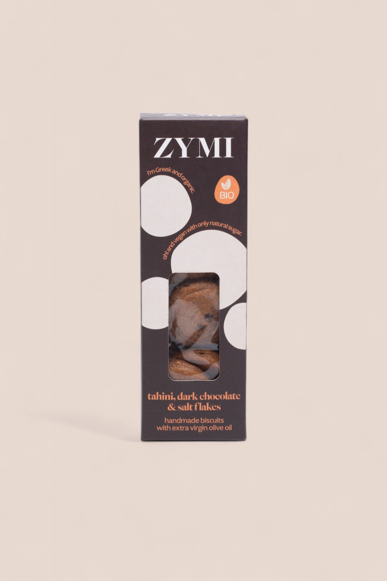 ZYMI product box in dark brown with white circles, showing tahini dark chocolate and salt flakes through a window cutout.
