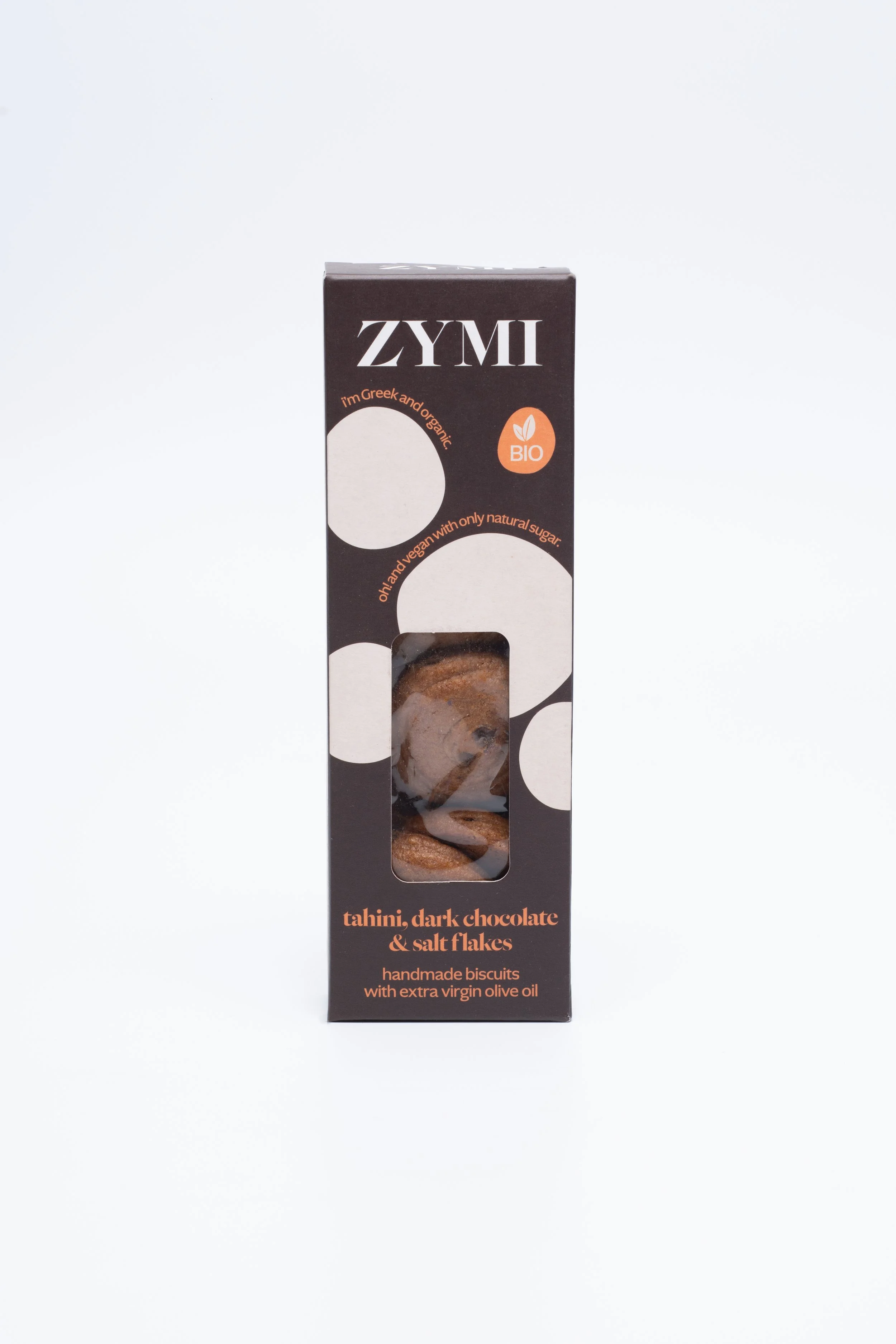 ZYMI product box in dark brown with white circles, showing tahini dark chocolate and salt falkes through a window cutout.