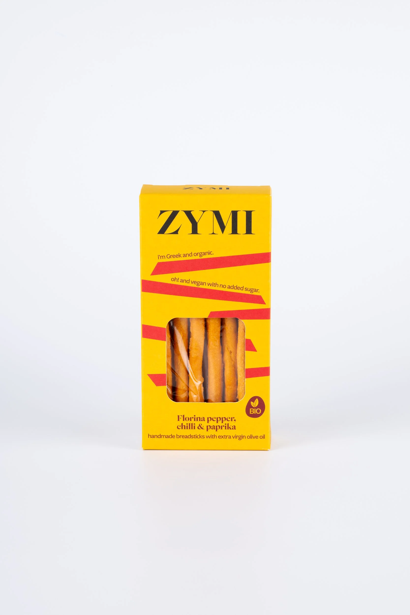 ZYMI product box in bright yellow colour with red lines, showing florina pepper, chili & paprika breadsticks through a window cutout.
