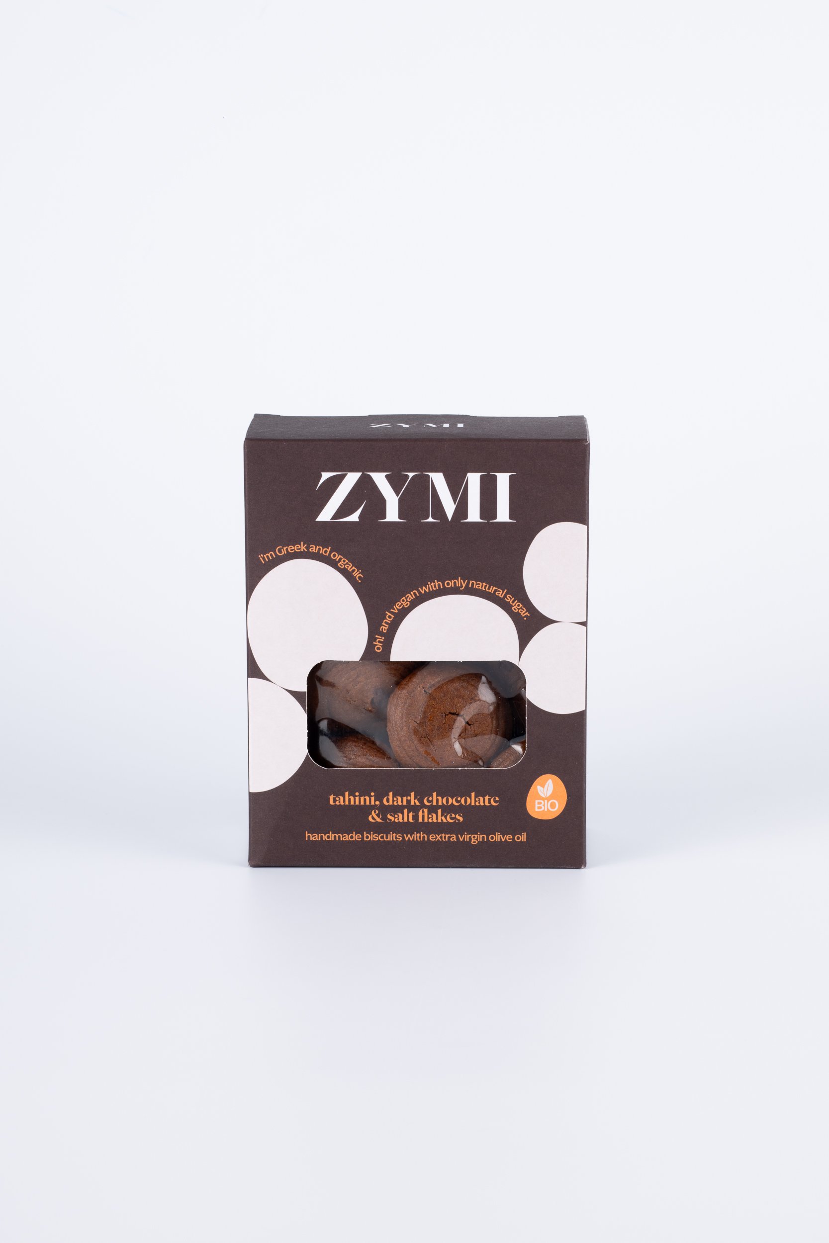 ZYMI product box in dark brown with white circles, showing tahini dark chocolate and salt falkes through a window cutout.
