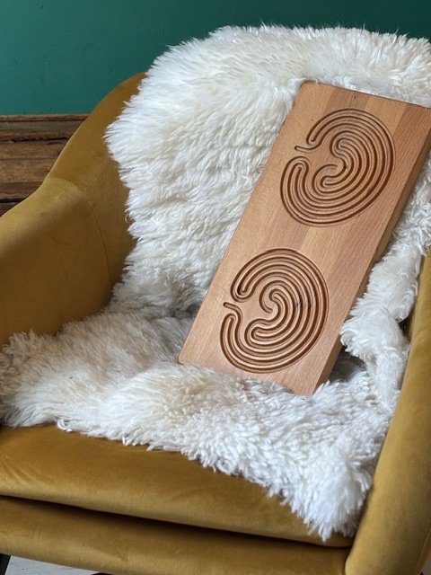 Een houten decoratie in de vorm van twee grote, gestileerde oren, geplaatst op een zachte, witte, schapenvacht die ligt op een gele stoel met een groene muur erachter.