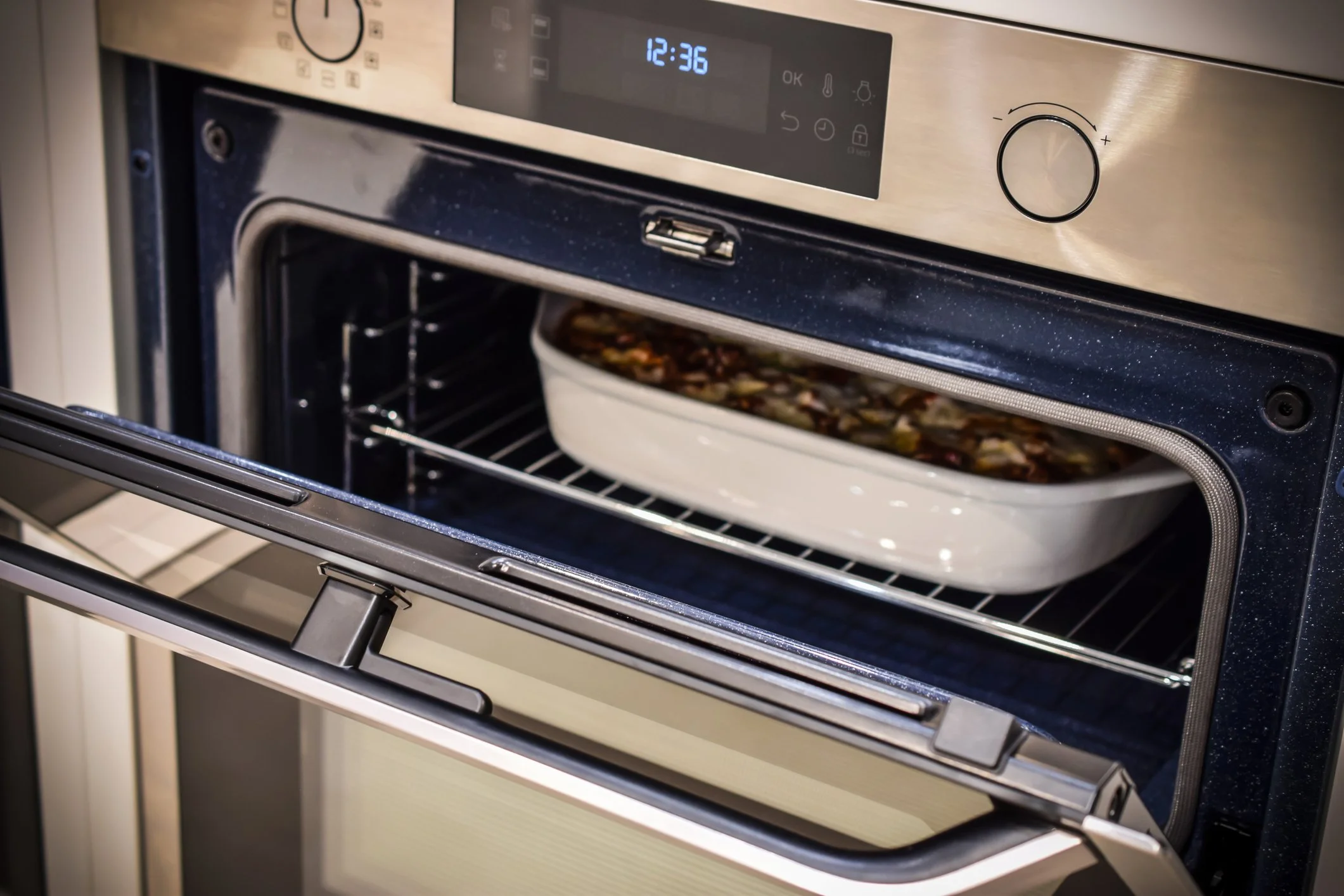 An oven with the door open, partially baking a dish in a white ceramic oven-safe dish inside.