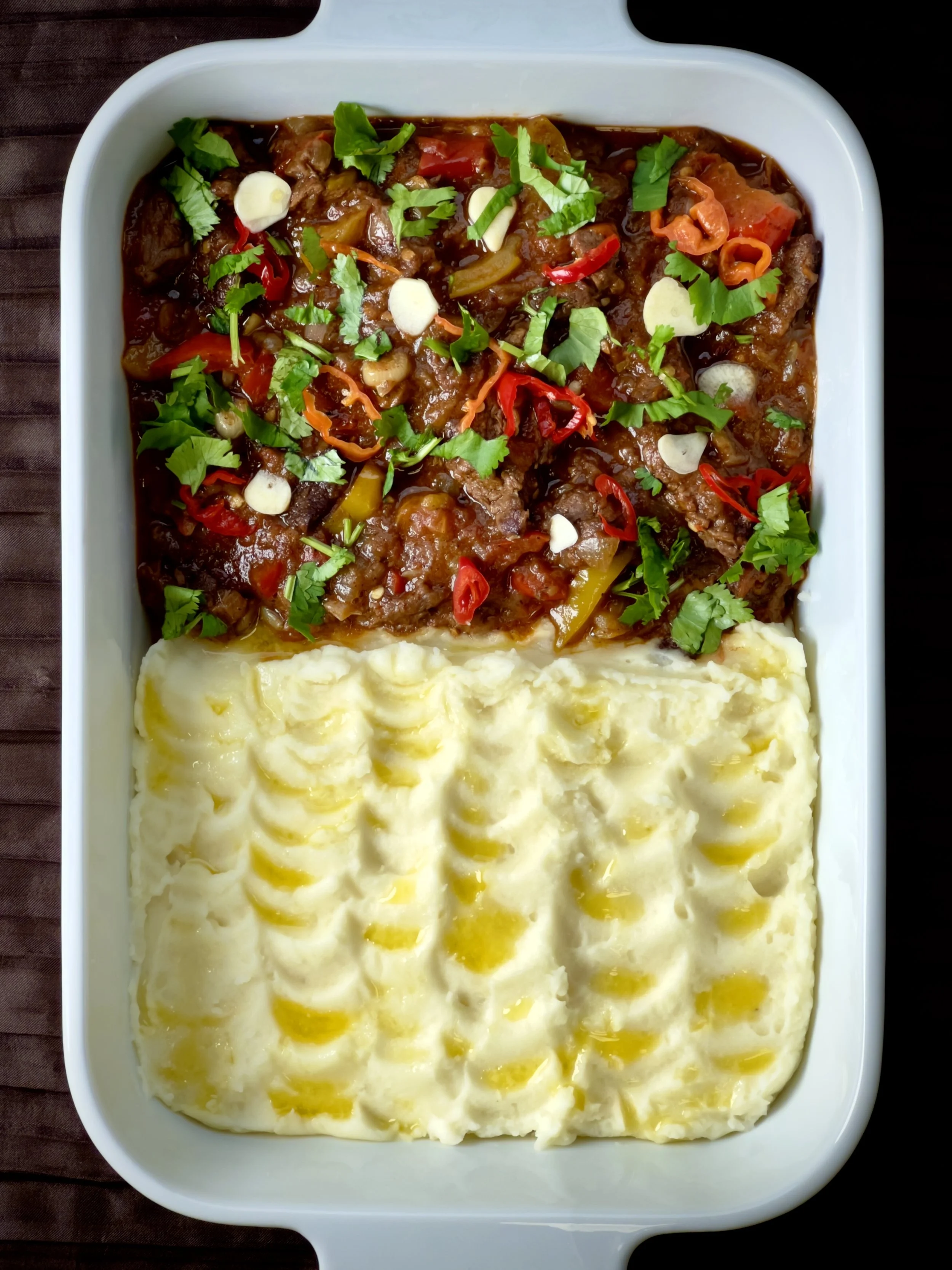 Beef stew with vegetables and garnished with cilantro and garlic, served with mashed potatoes.