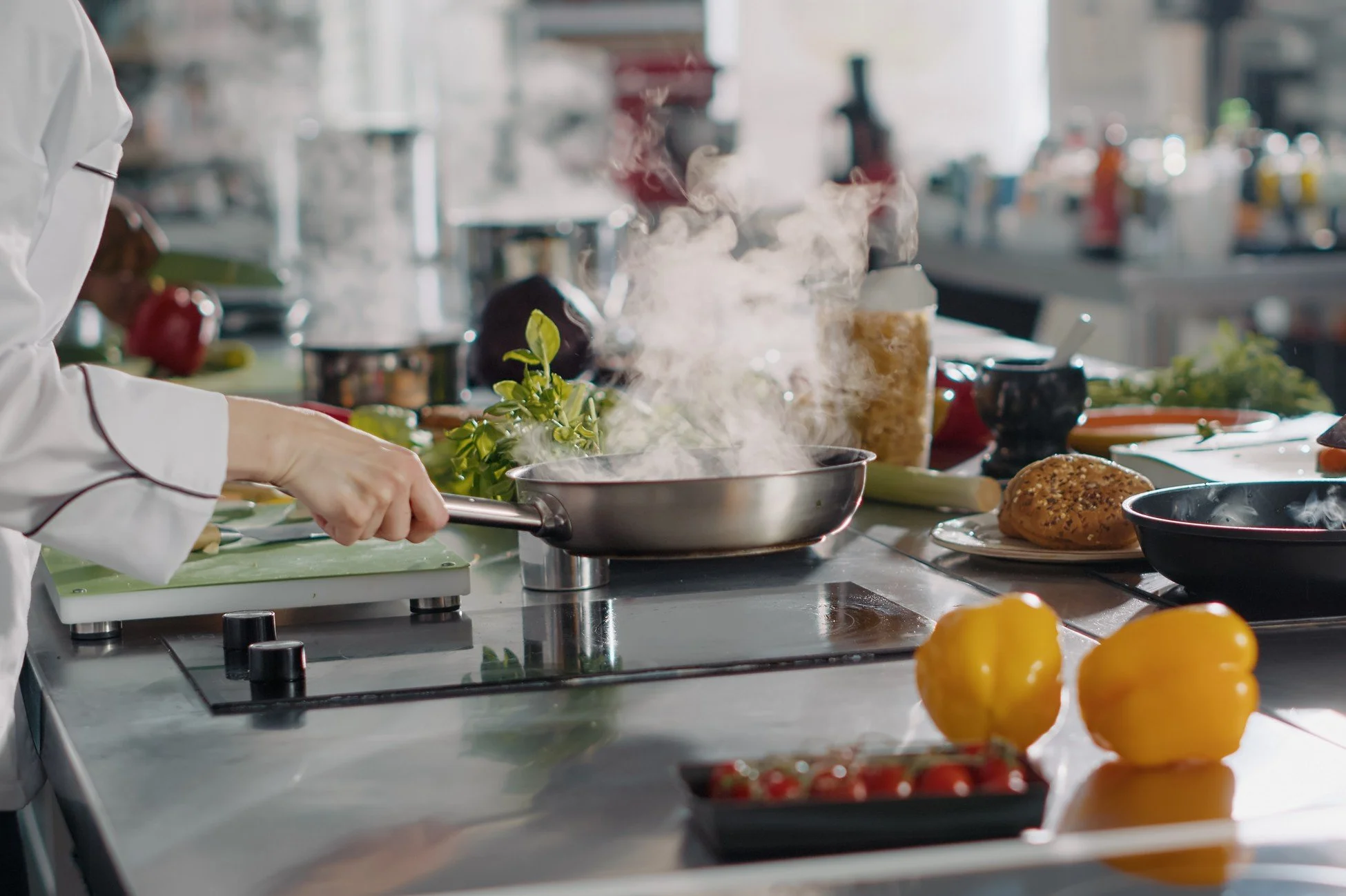 A person cooking on a stovetop with steam rising from a pan, surrounded by fresh vegetables and kitchen utensils in a modern, bright kitchen.