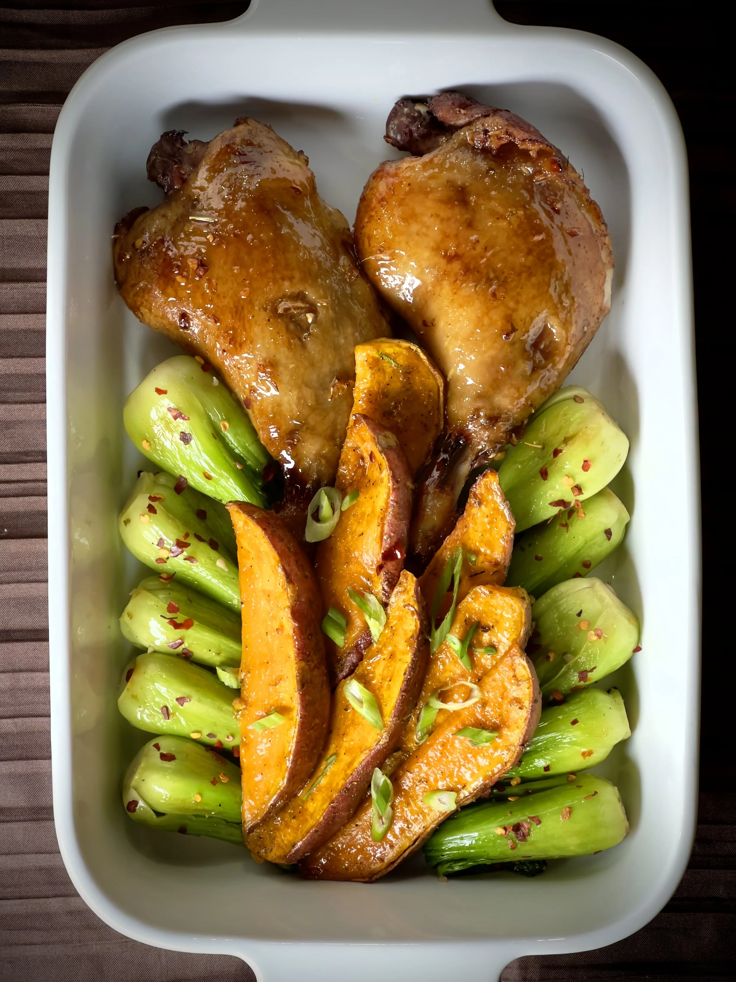Roasted chicken thighs with glazed butternut squash and bok choy garnished with sliced green onions and red pepper flakes in a white serving dish.
