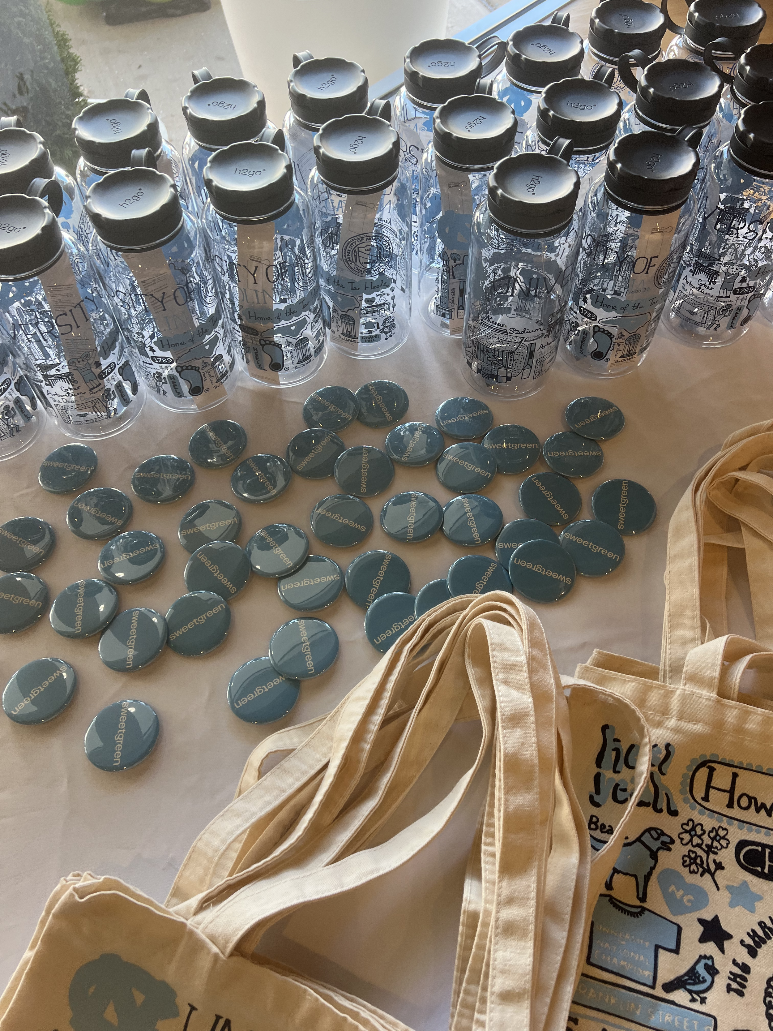 Collection of water bottles, buttons, and tote bags with Charlotte, North Carolina-themed graphics and text