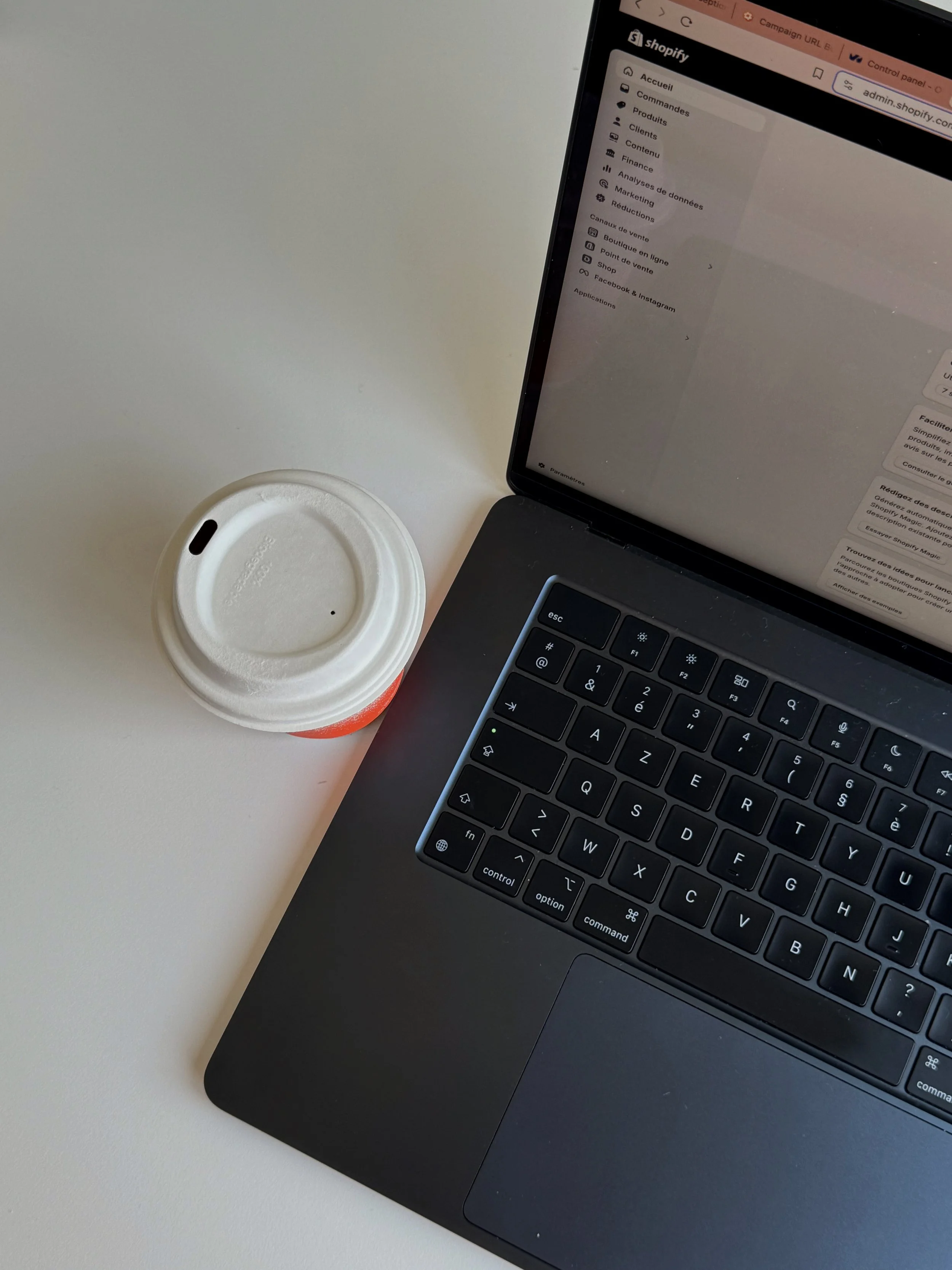 A laptop on a white desk with a cup of coffee beside it.