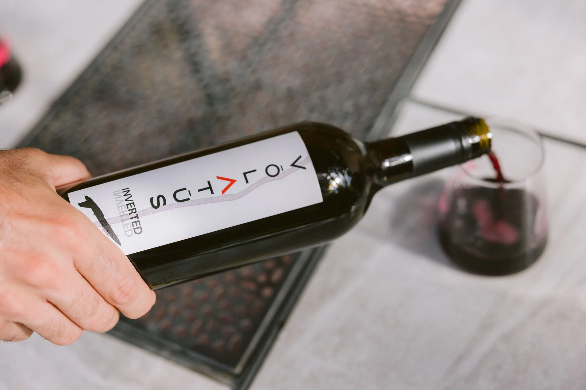 Person pouring red wine from a bottle labeled "VOLATUS" into a glass on a table.