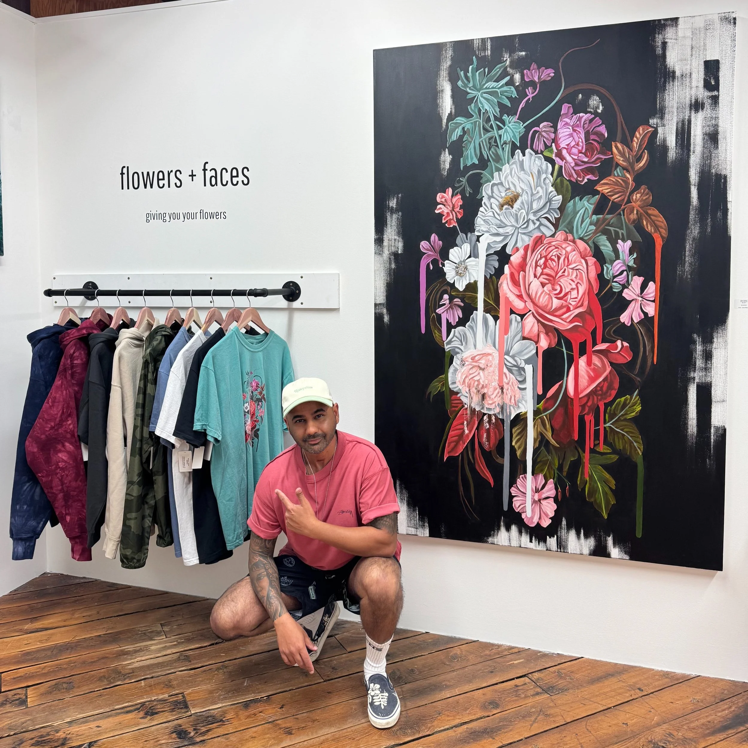Man posing in front of a floral painting and clothing rack