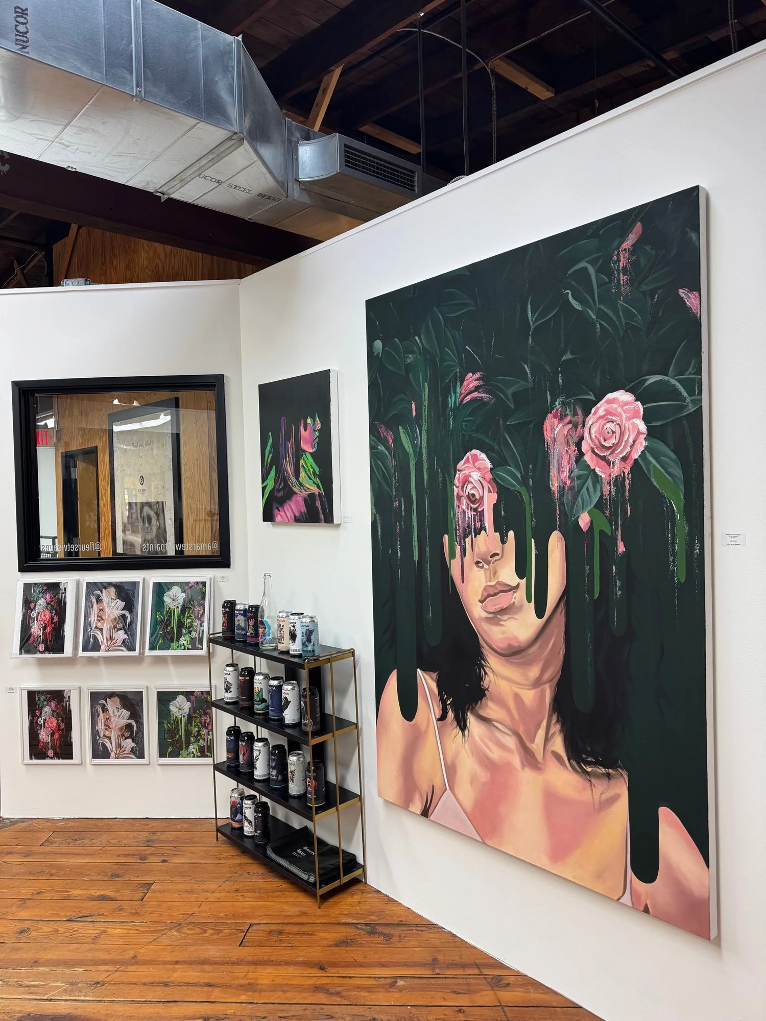 Art gallery interior with various paintings on display, including a large painting of a woman with roses and dripping green paint on her face. Adjacent artwork and shelves with cans are also visible.