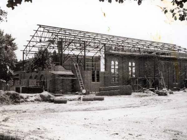 Black and white photo of a building under construction with a metal framework and scaffolding around it.