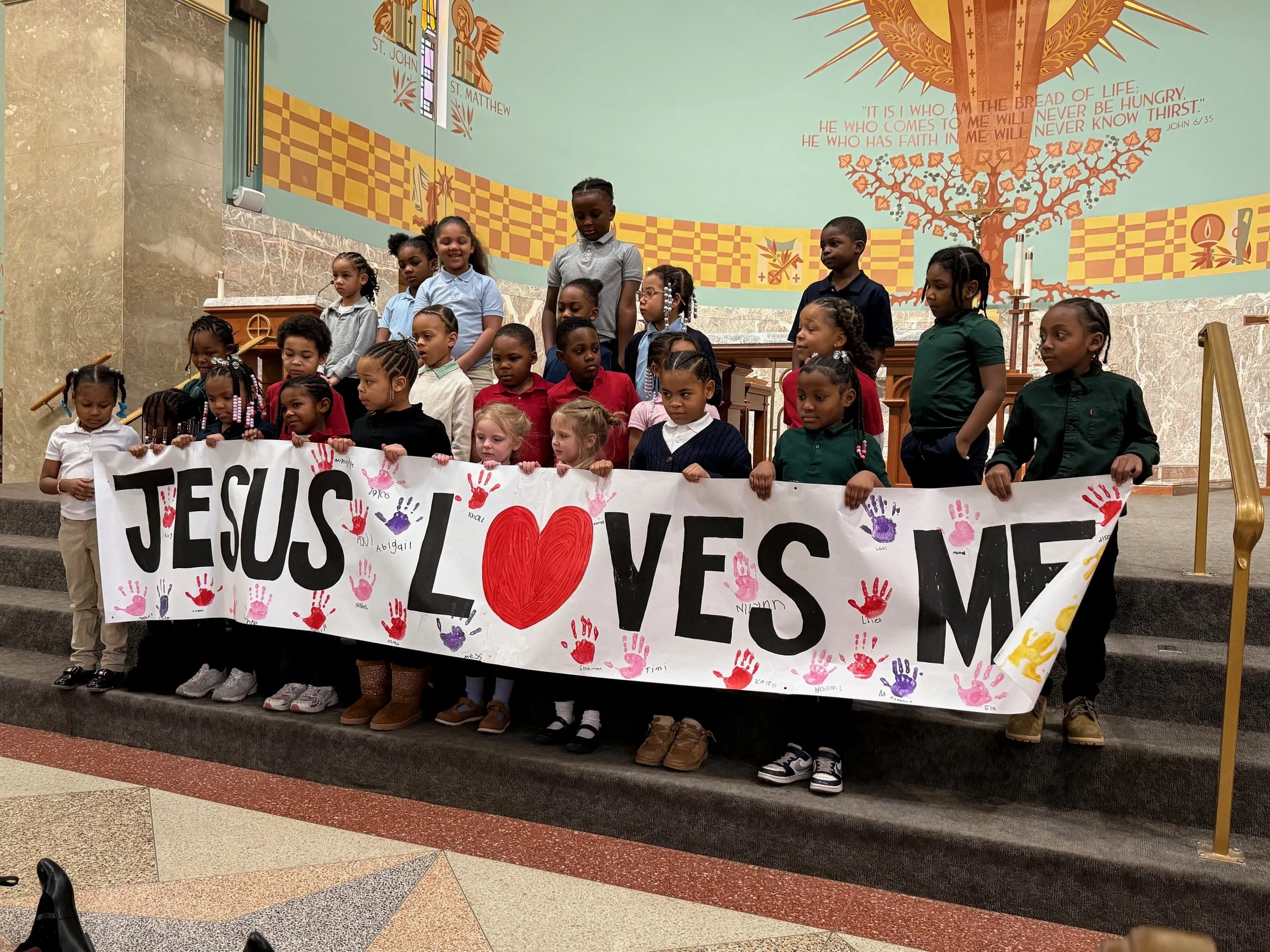 An image of children holding a sign that says "Jesus loves me" in a church