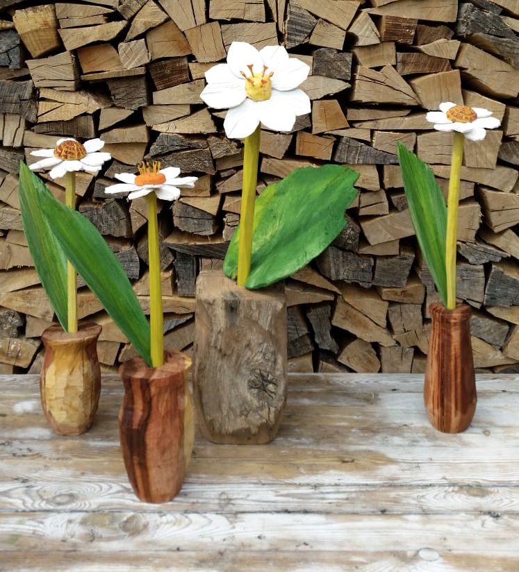 Holzskulpturen von Blumen in Vasen vor einem Stapel Holzkisten.