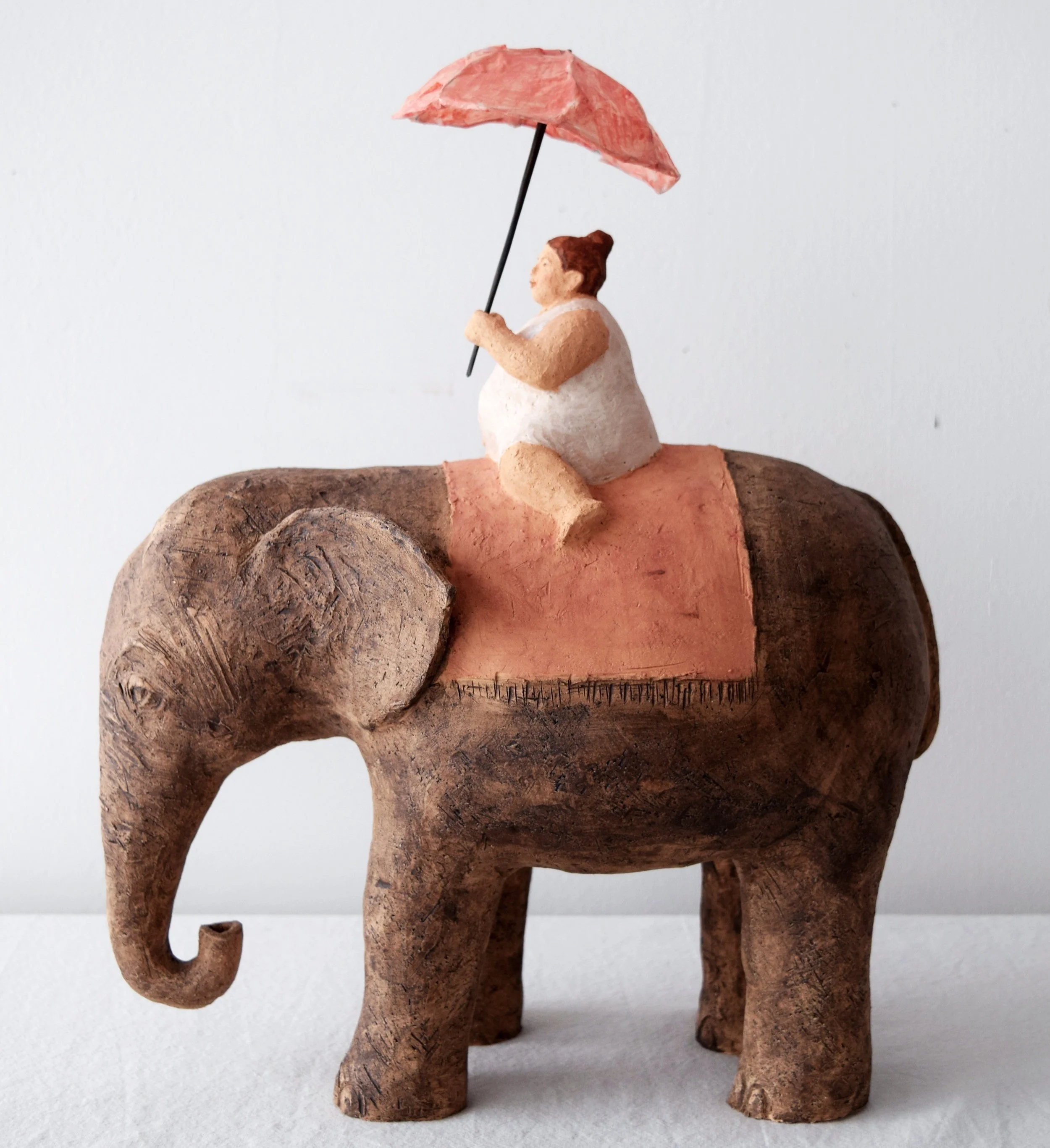 Kunstwerk einer Elefantenfigur mit rotem Sattel, auf dem eine menschliche Figur mit einem roten Regenschirm sitzt.