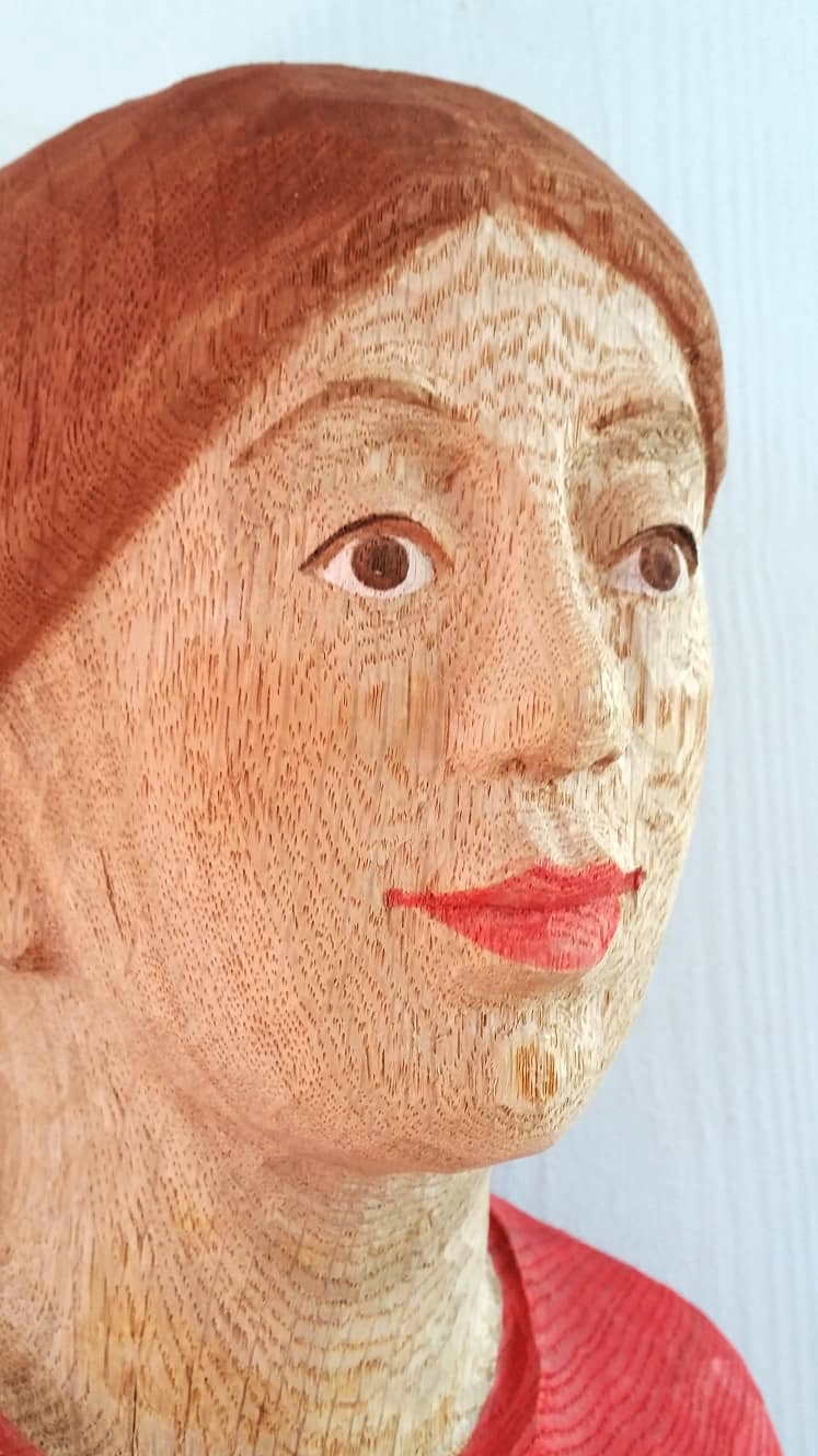 Holzskulptur eines weiblichen Gesichts, detailliert geschnitzt mit roten Lippen und braunen Haaren.