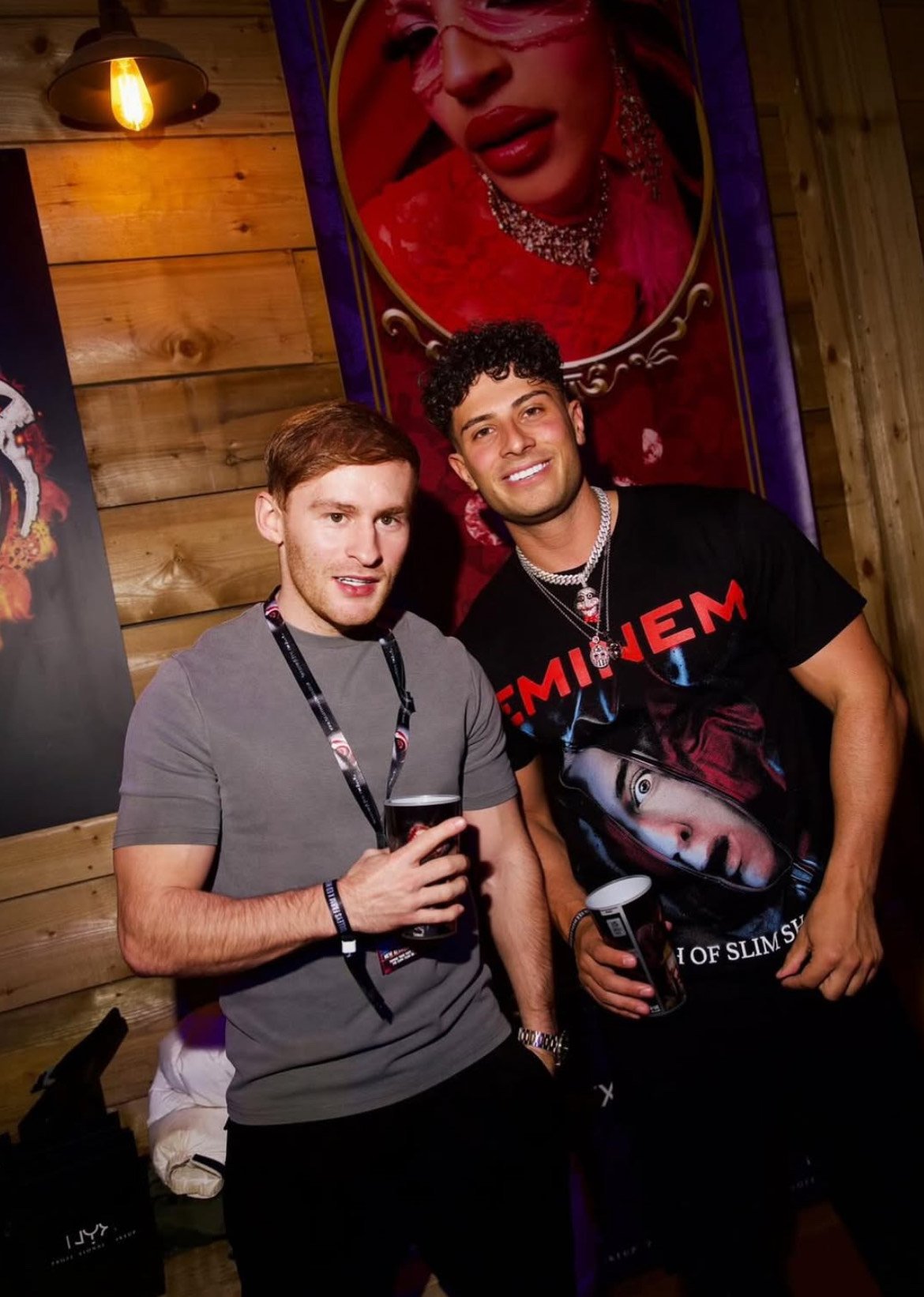 Two women standing in front of a black backdrop with the logo 'Thorpe Park'. They are posing for a photo, smiling, with grey and black casual outfits.
