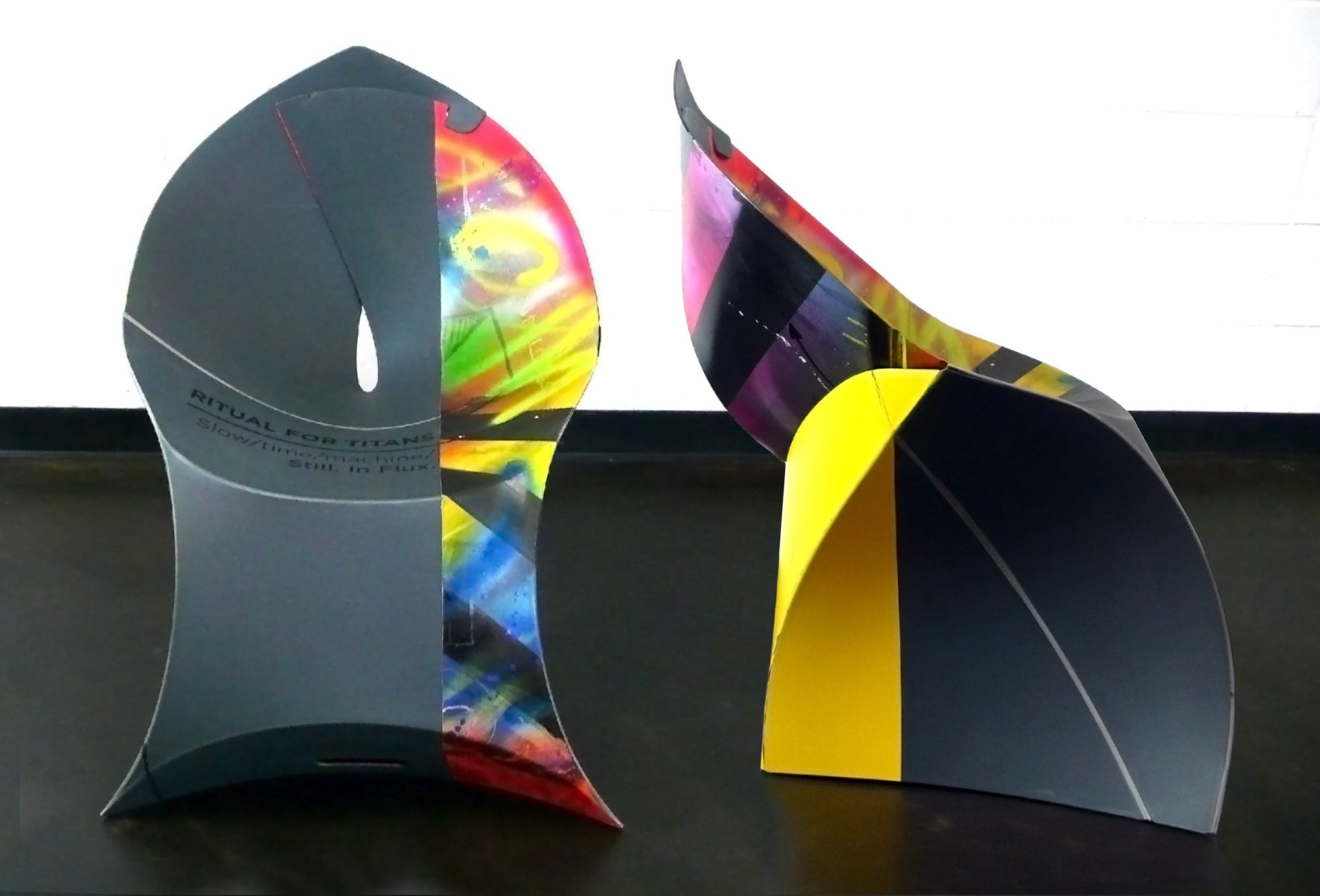 Modern art sculpture with colorful geometric design and abstract shapes on a dark floor and white wall background.