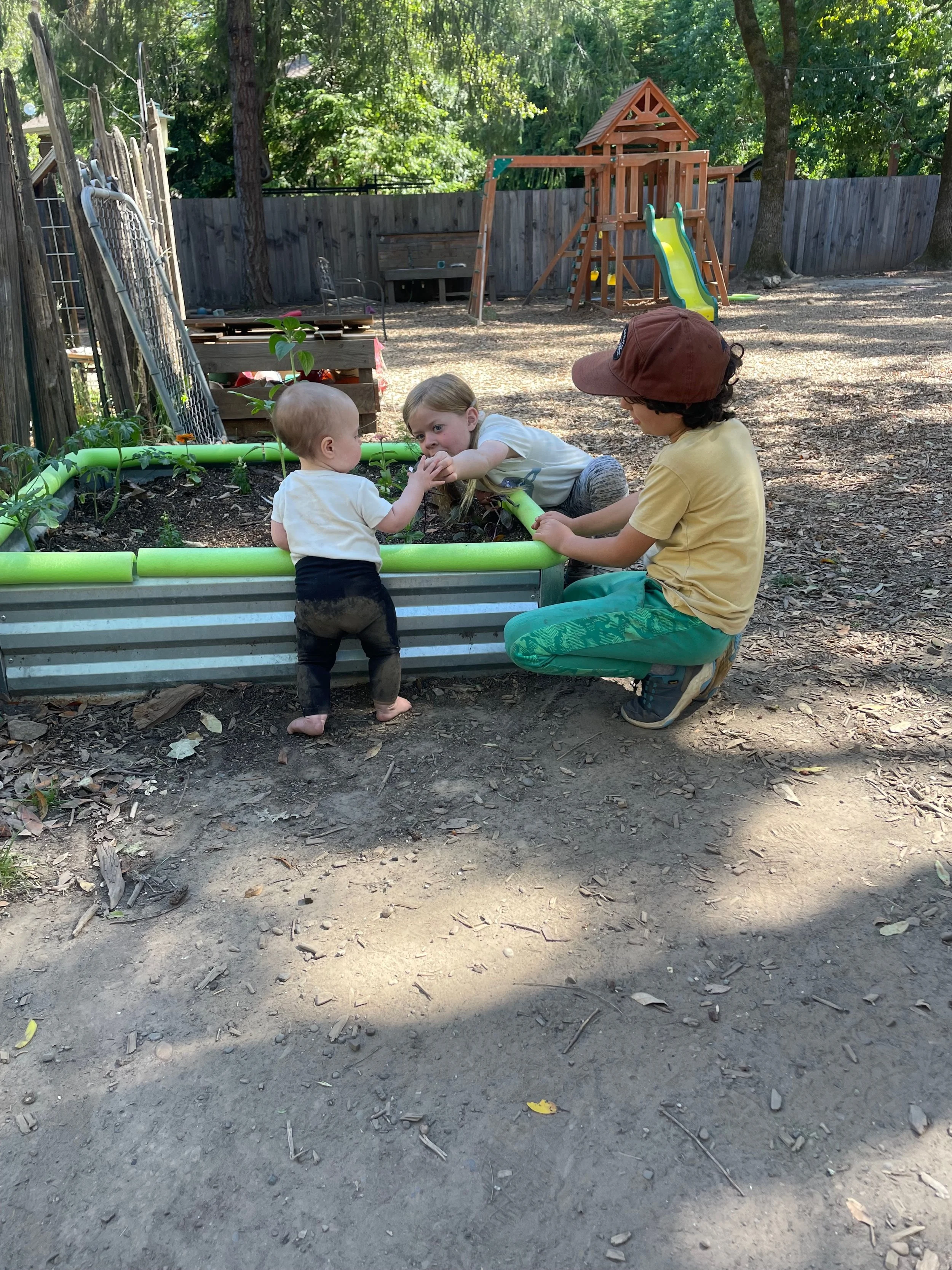 Playing with plants in a backyard garden, with playground equipment in the background.