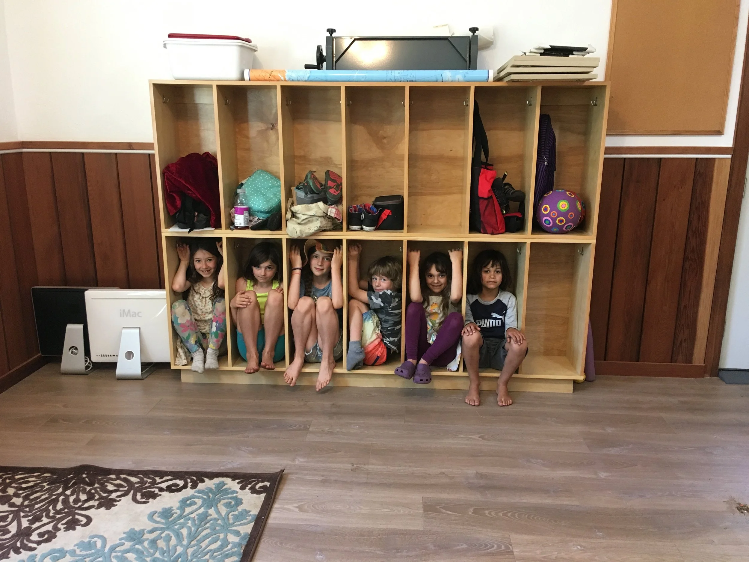 Six children sitting inside cubby shelves in a room.