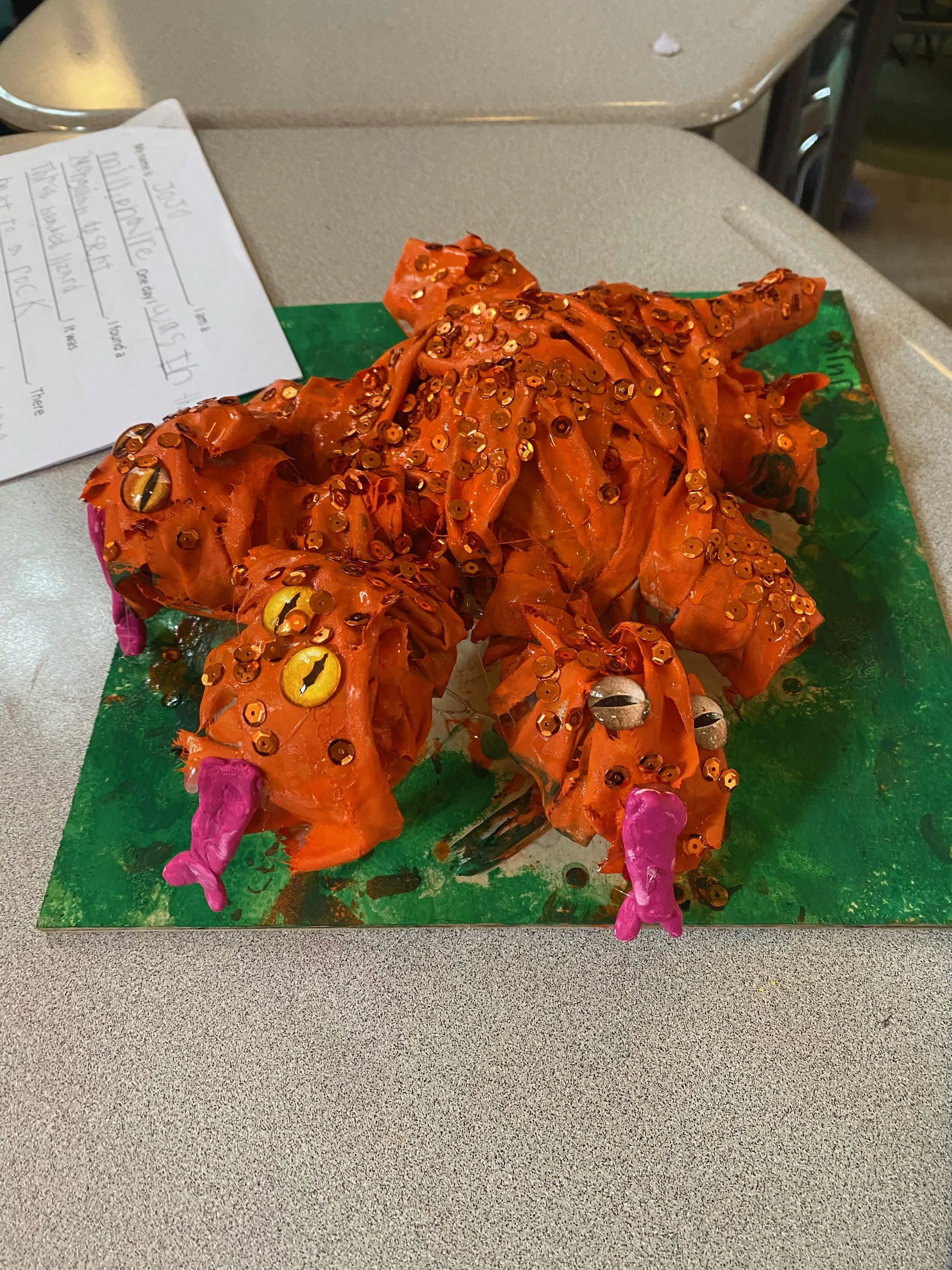 Final project of a spider made with orange material, decorated with sequins and googly eyes, with purple legs.