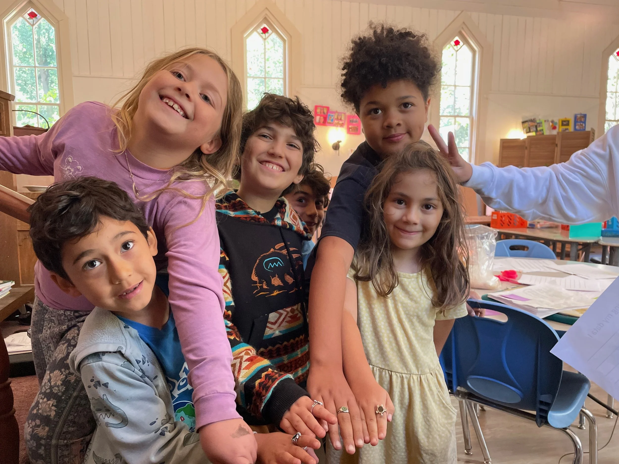 Happy children in a classroom, showing their hands together, smiling.
