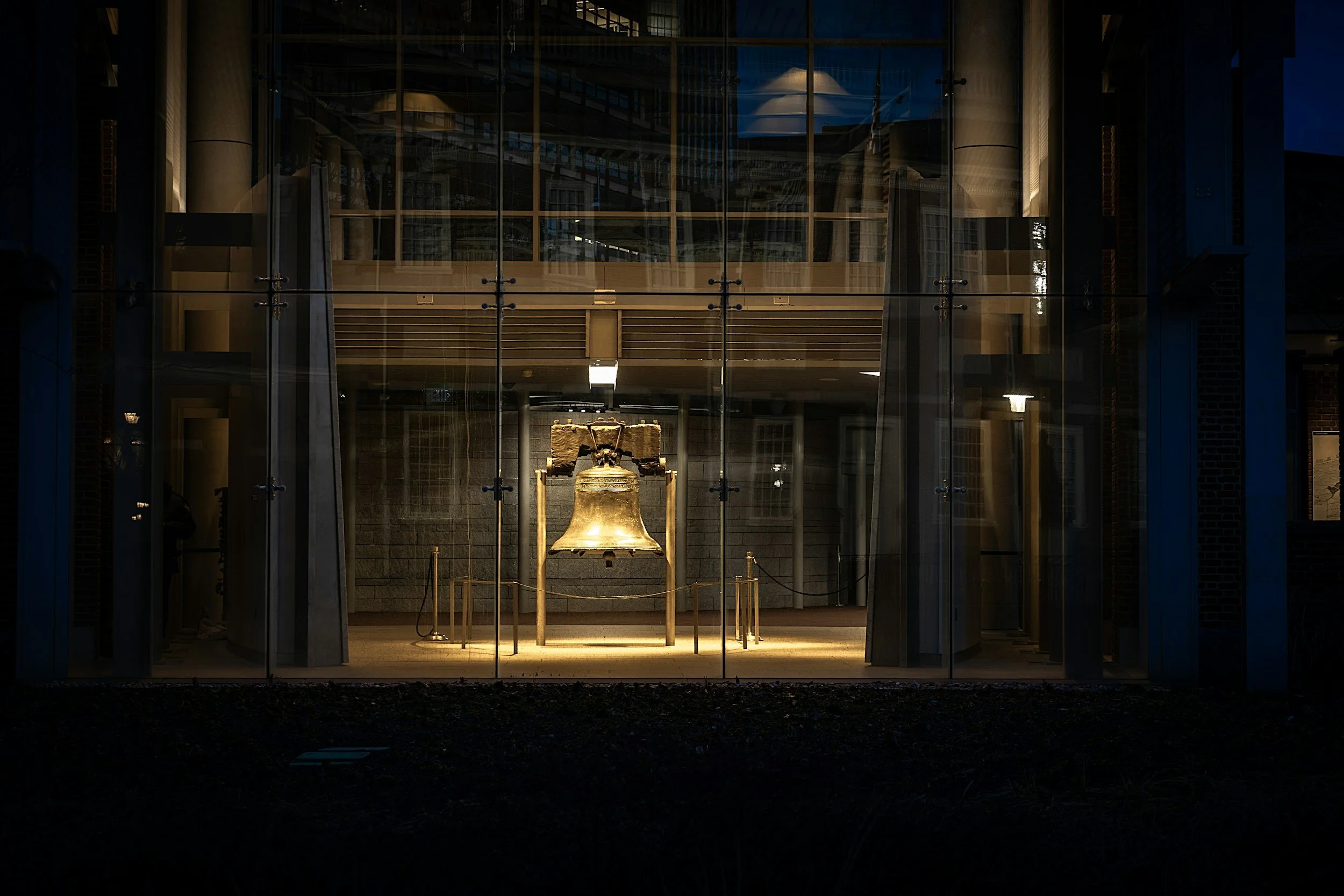 Night view of a modern glass building with a large bell inside, illuminated from below, seen through the glass facade.
