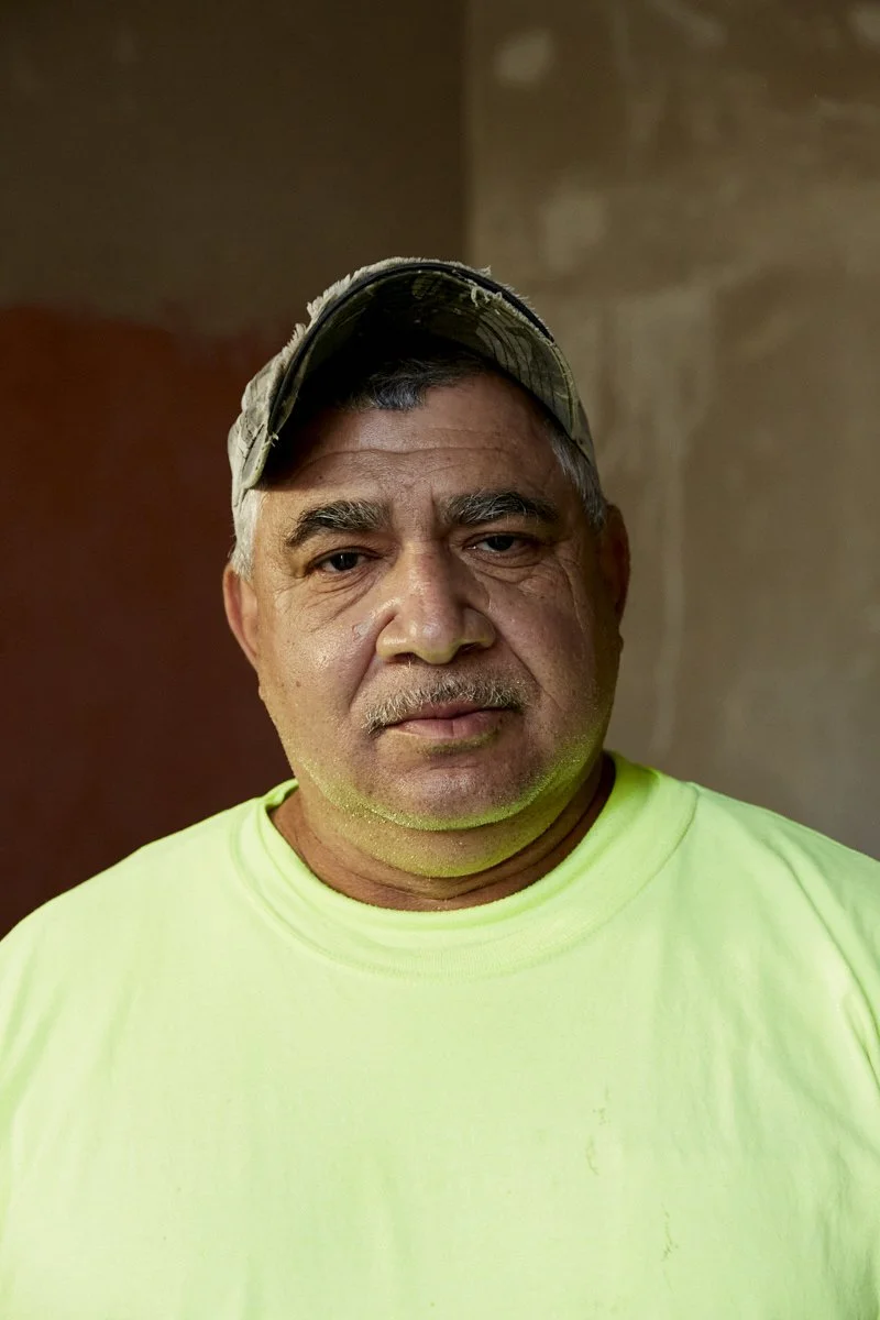 A middle-aged man wearing a camouflage baseball cap and a bright yellow shirt, standing indoors against a plain background. Roy Gaillard fourth generation plasterer New Orleans.