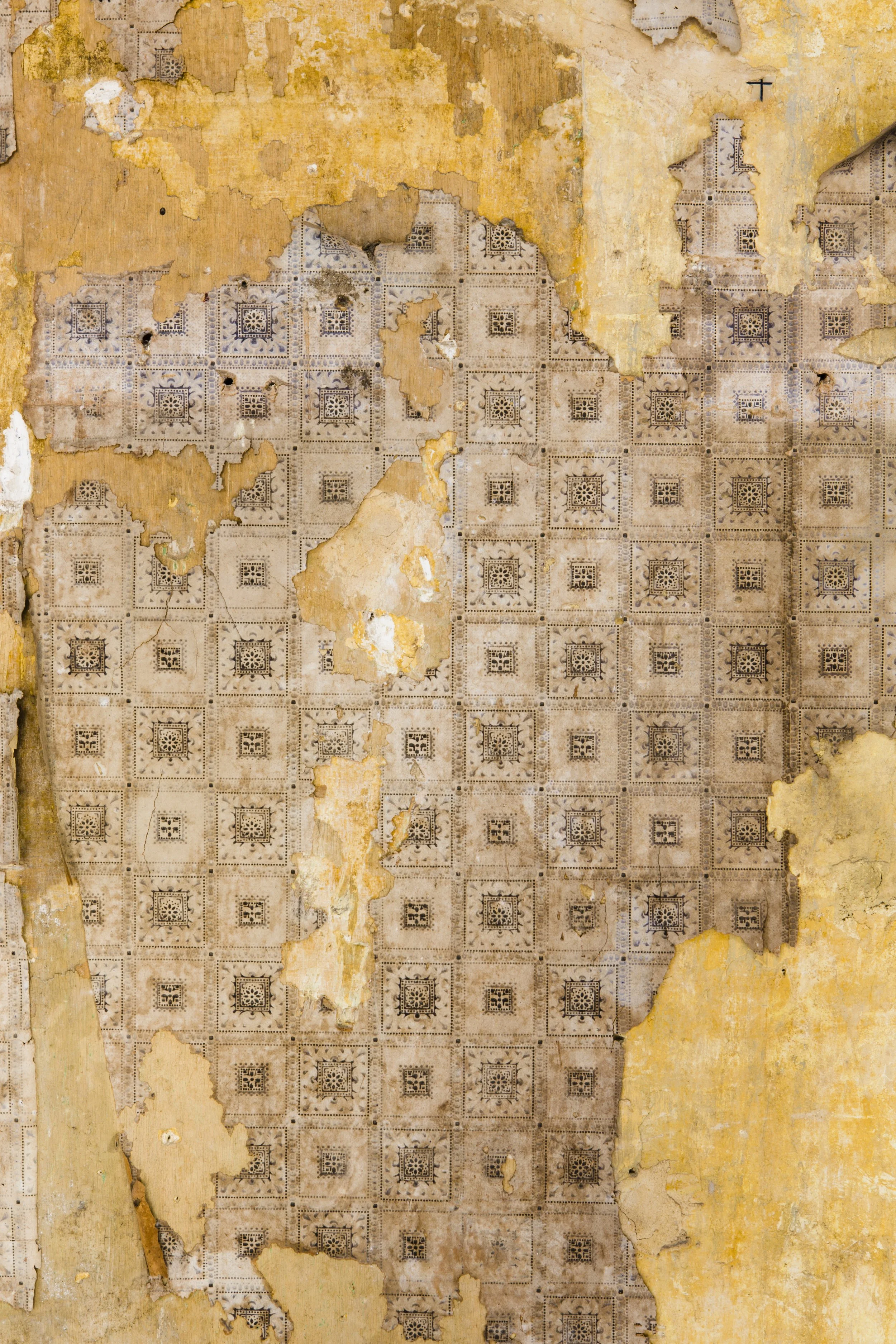 Peeling old wallpaper with a faded, intricate geometric pattern in shades of brown and beige on the wall.